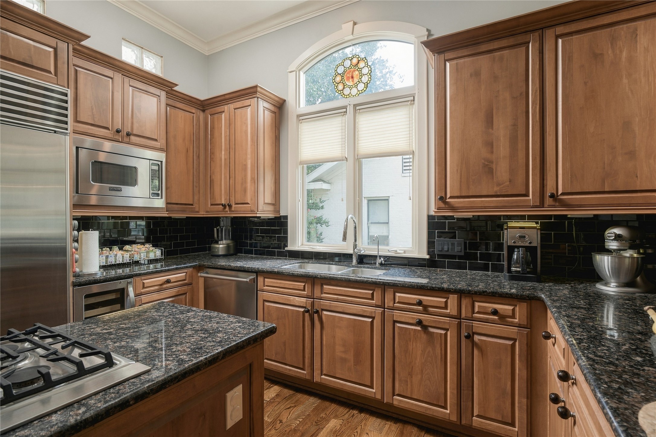 The kitchen shifts the palette warmer with rich wood cabinetry, dark granite surfaces and a black tile backsplash, while an arched window brings natural light over the sink.