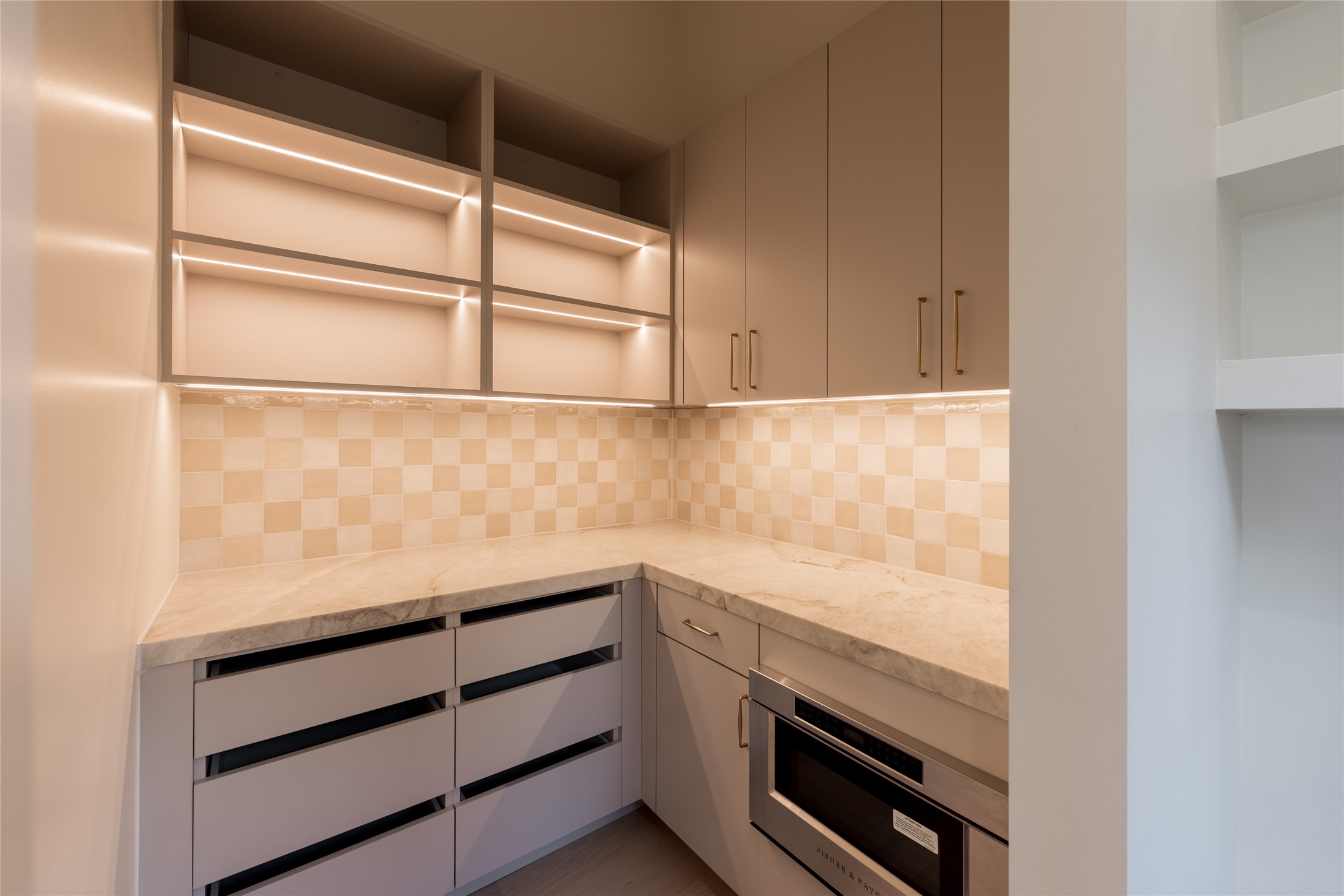 Integrated lighting turns the butlers pantry into a design moment of its own, illuminating generous cabinetry, natural stone counters and dedicated prep space while keeping the working side of the kitchen discreetly tucked away.