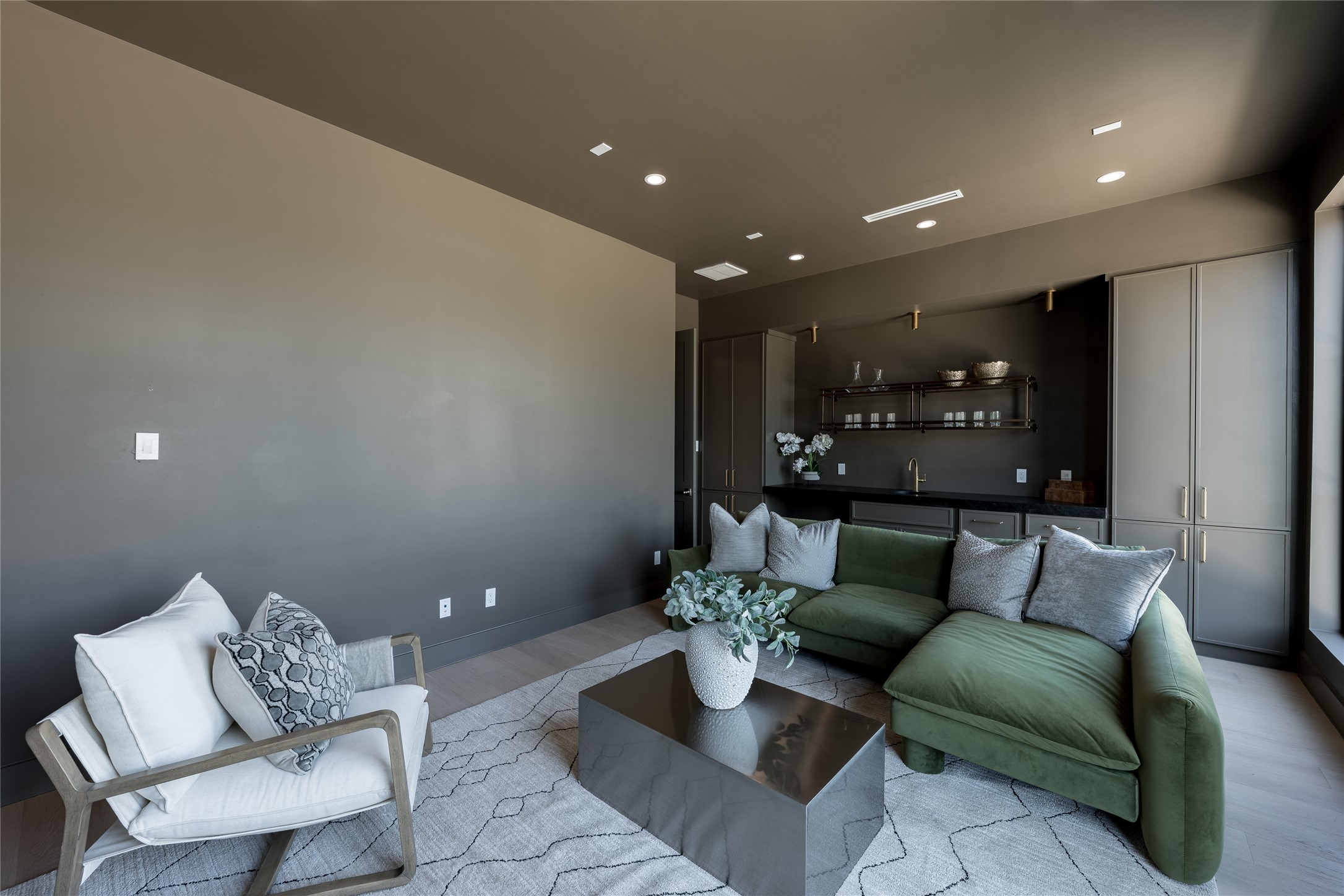 A second perspective of the media room reveals a thoughtfully appointed lounge, where rich, moody tones meet relaxed comfort. Custom cabinetry, an integrated beverage station, and warm metallic accents create a sophisticated setting for entertaining or unwinding.