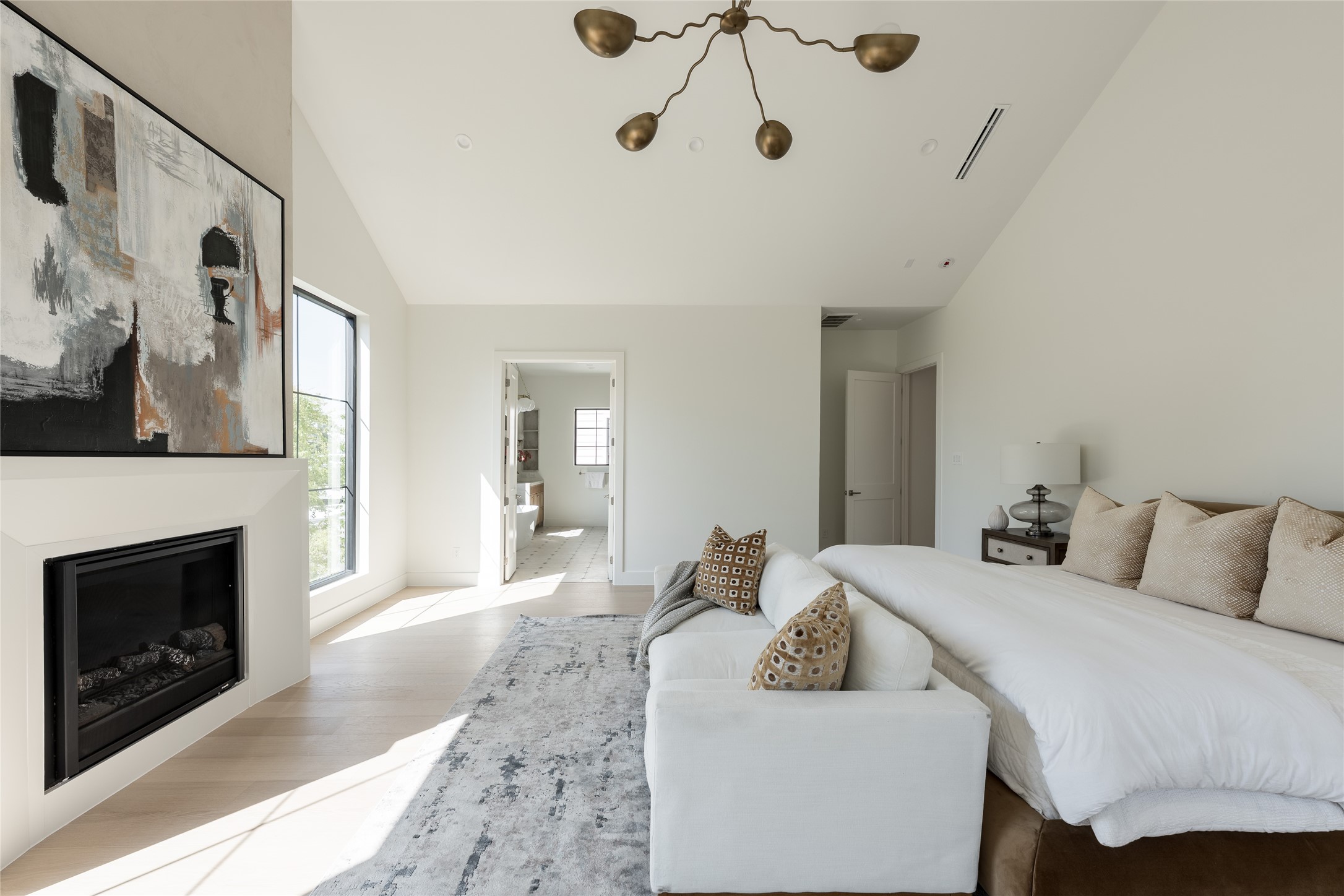 An intimate sitting area and sleek fireplace bring warmth and dimension to the primary bedroom. Just beyond, the primary bath extends the experience with a continuation of the home's refined finishes and considered details.