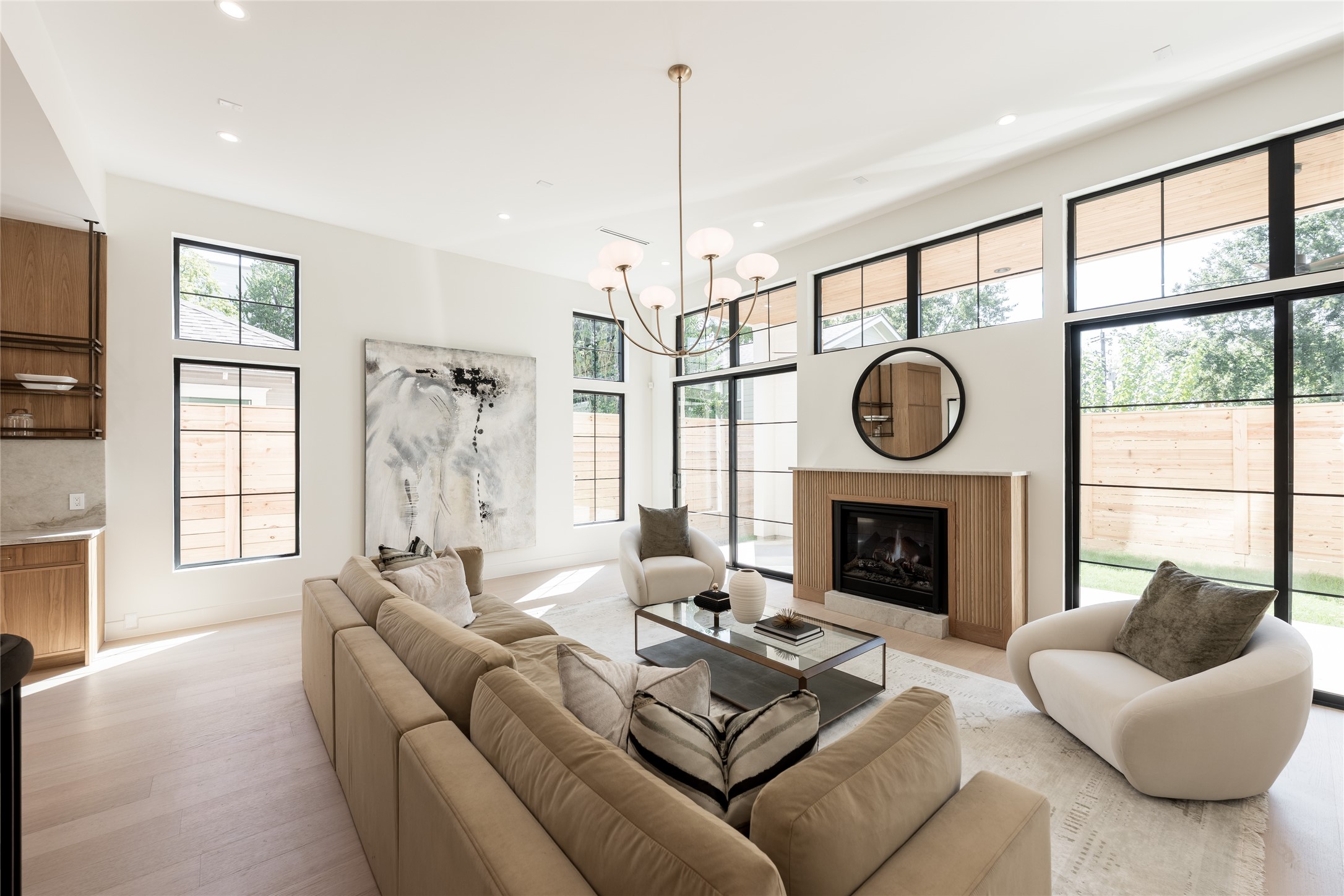 The great room balances dramatic scale with warmth, pairing 12 foot ceilings and a fluted fireplace with walls of grid windows that bring natural light deep into the space.