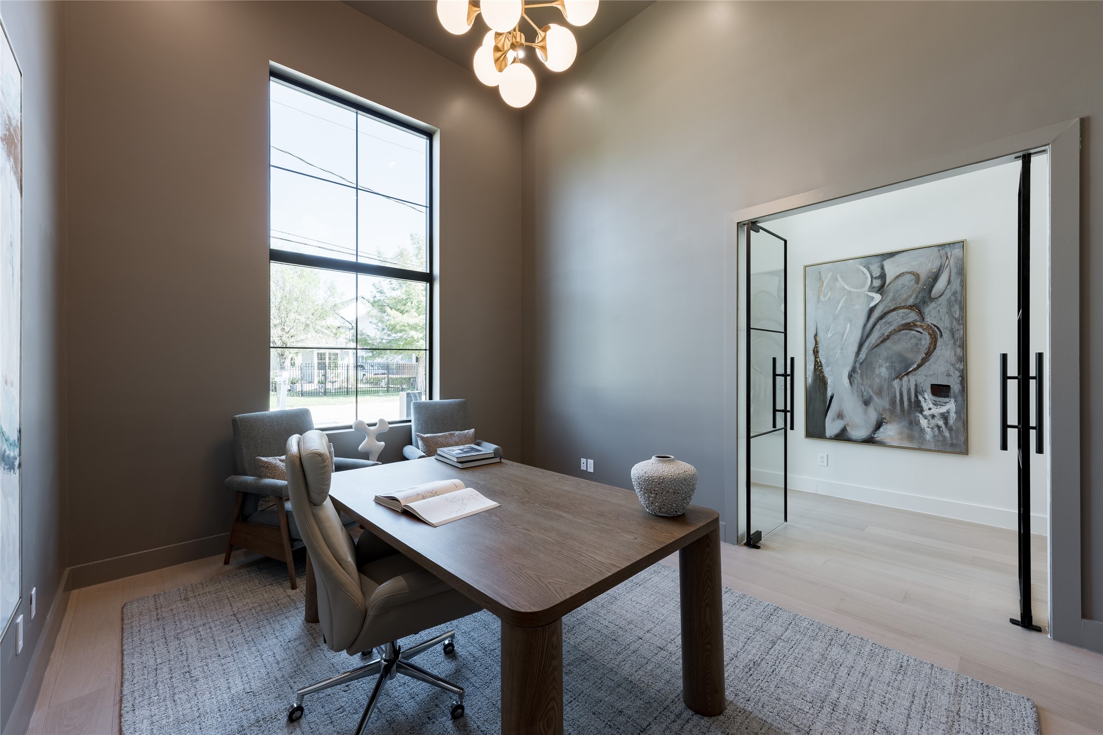 The private study pairs a dramatic 15 foot ceiling with glass walls that preserve the homes sense of openness, while a concealed bookcase door adds an unexpected layer of privacy.