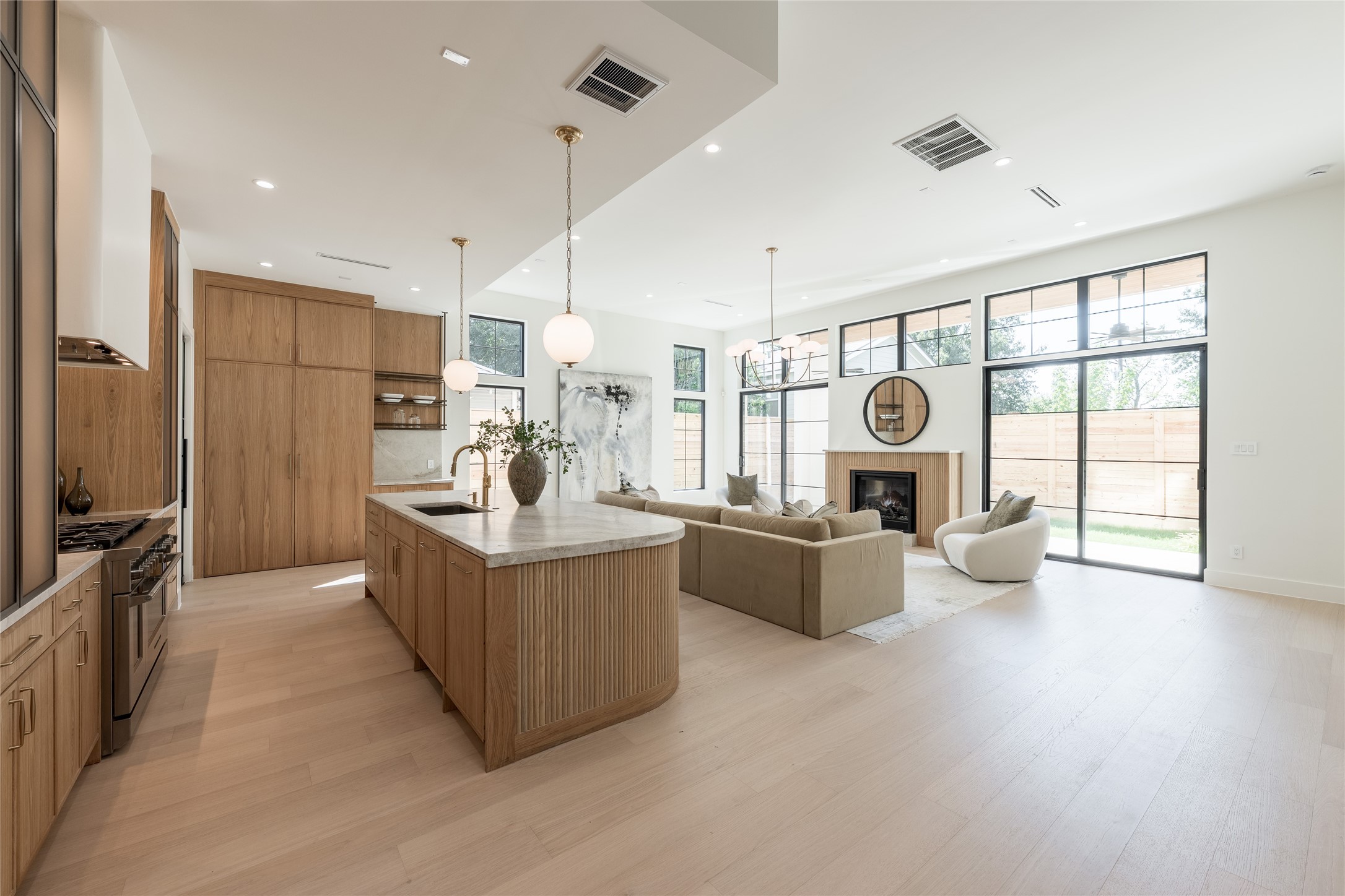 Integrated cabinet lighting highlights the custom white oak cabinetry and sculptural hood, while the kitchens open exposure to the soaring dining room creates a striking visual connection between the two spaces.