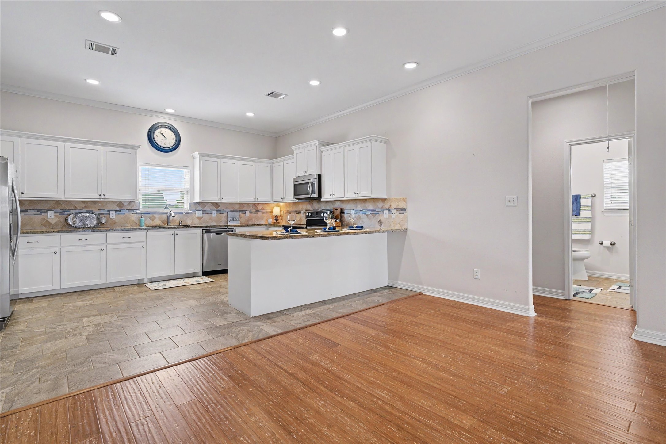 The coastal-inspired white kitchen radiates elegance and charm, featuring sleek cabinetry and modern appliances. At the heart of this space is a large peninsula breakfast bar, perfect for casual dining or entertaining guests