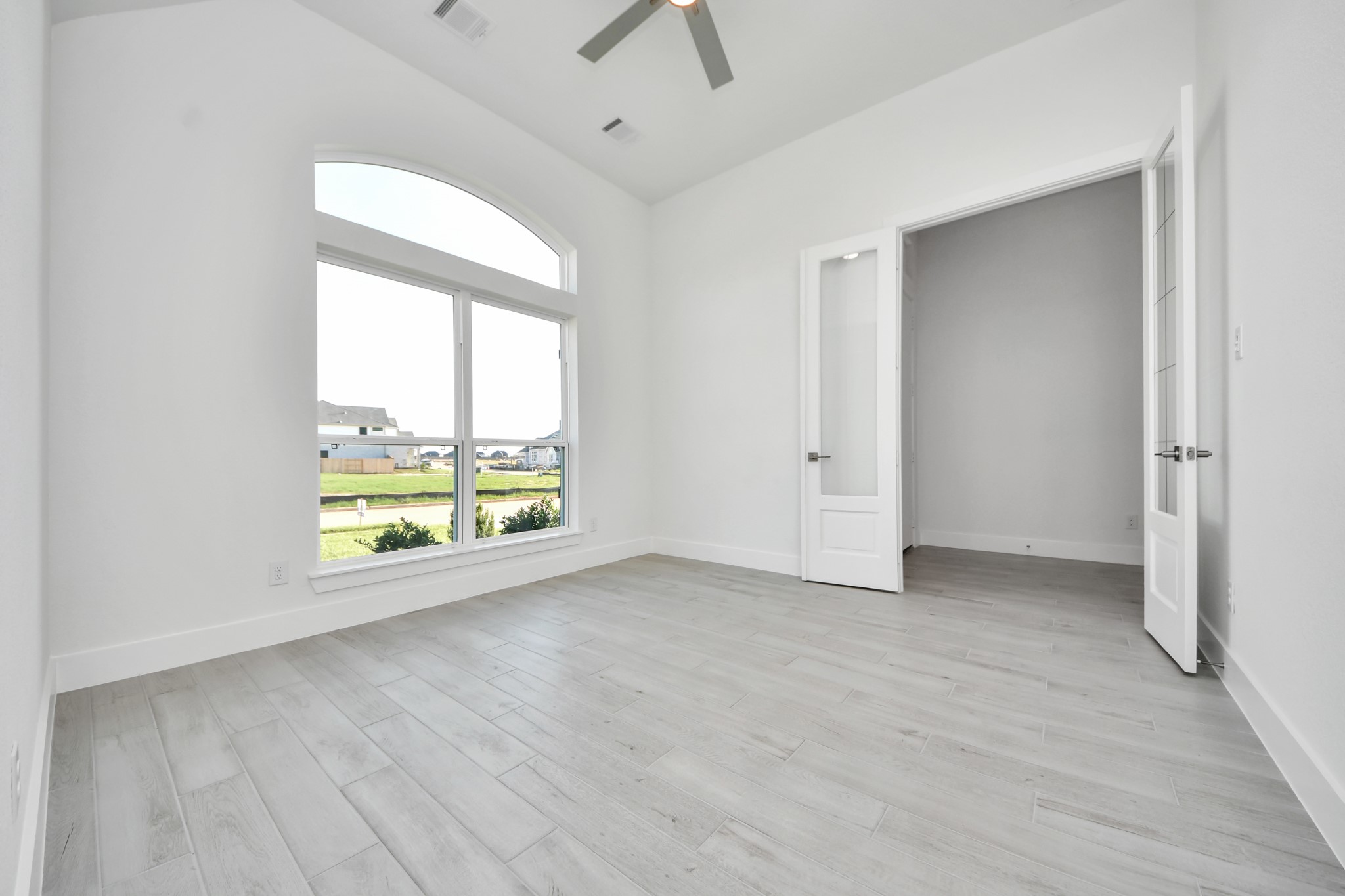 Experience the perfect blend of sophistication and warmth in this home office, boasting elegant wood-look tile flooring and flooded with natural light from expansive windows and French doors.