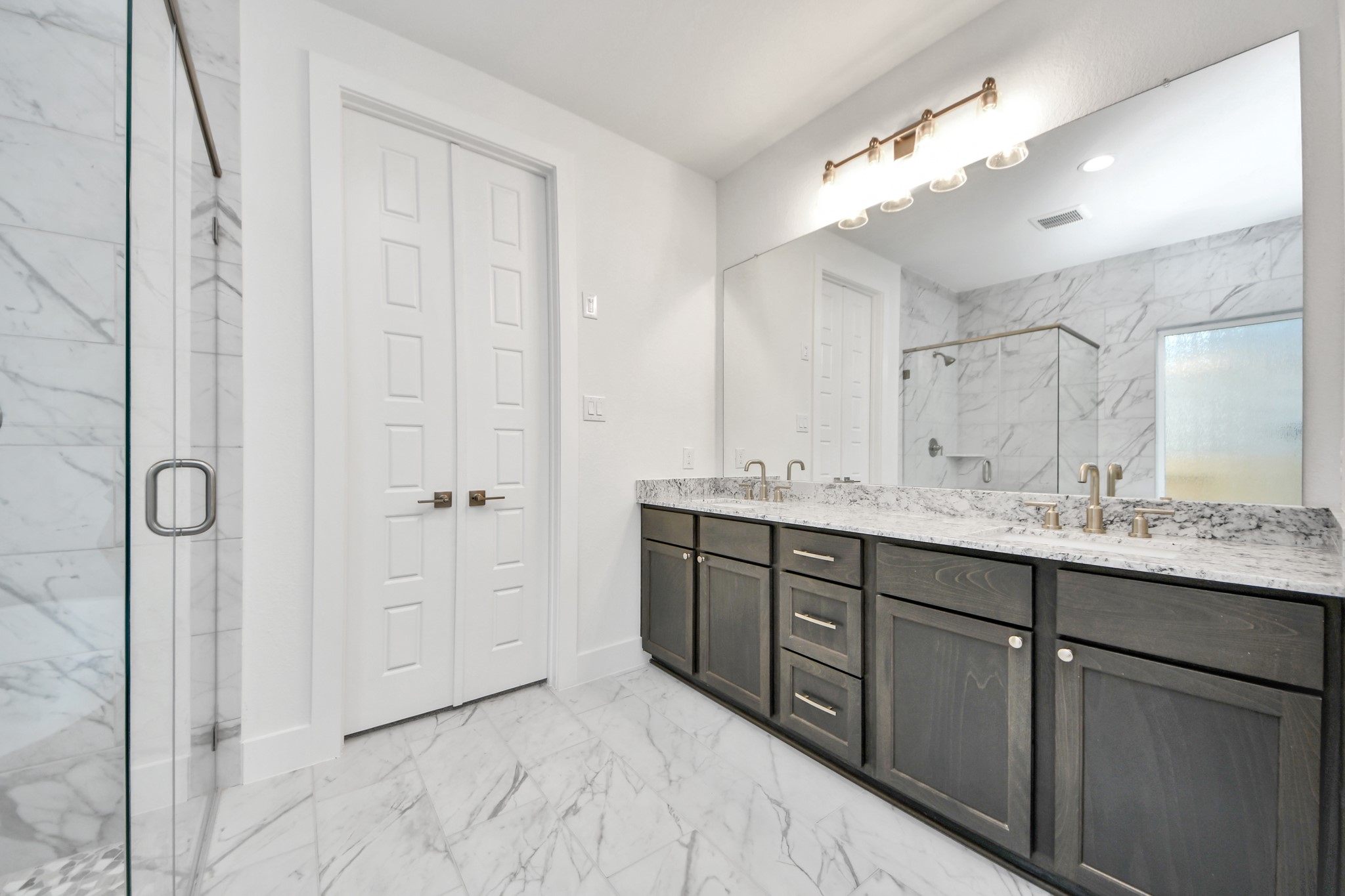 Elevate your daily routine at the elegant vanity, now equipped with double sinks, light countertops, modern hardware, and beautiful vanty lights.