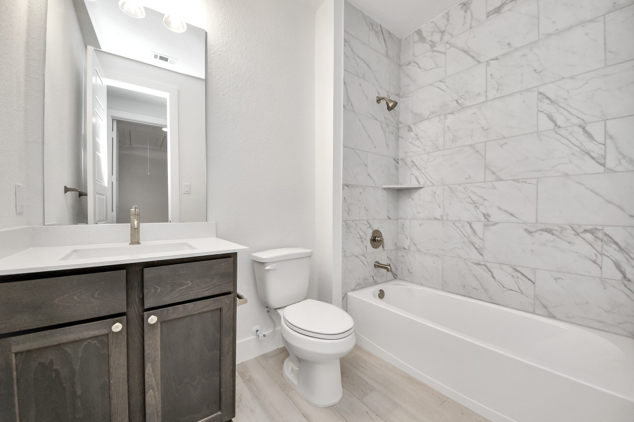 Secondary bath features tile flooring, bath/shower combo with tile surround, light stained wood cabinets, beautiful light countertop.