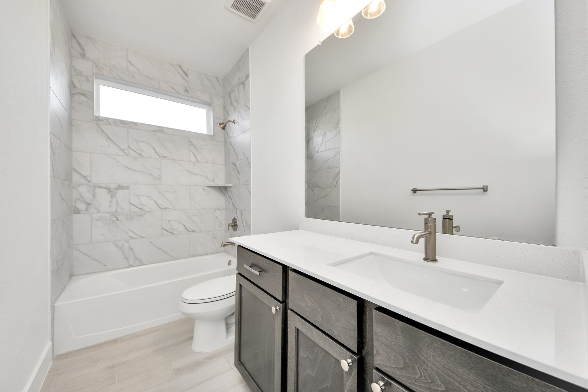 Secondary bath features tile flooring, bath/shower combo with tile surround, light stained wood cabinets, beautiful light countertop.