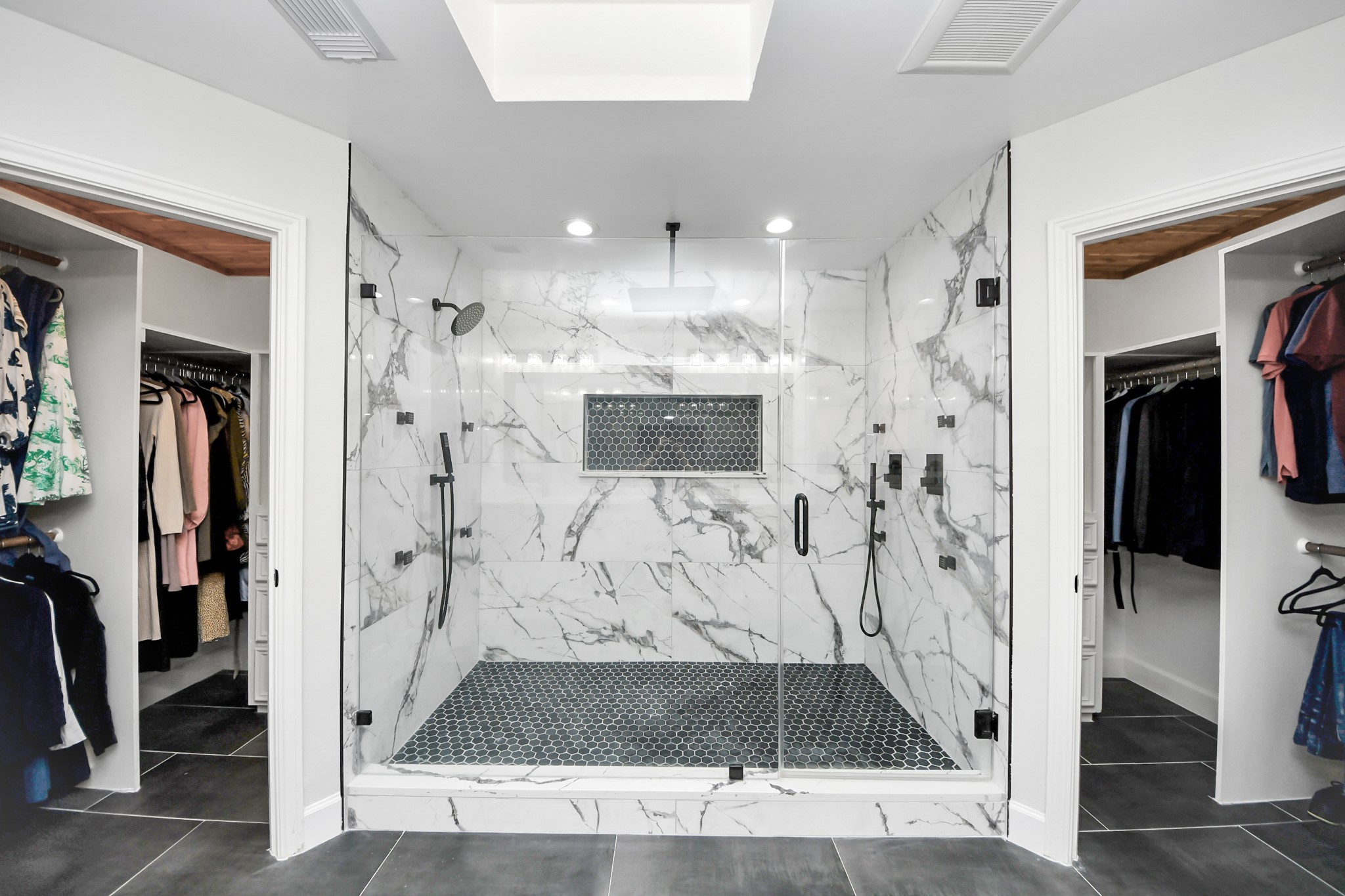 Luxurious marble shower with dual rain shower heads and modern fixtures, flanked by spacious walk-in closets.