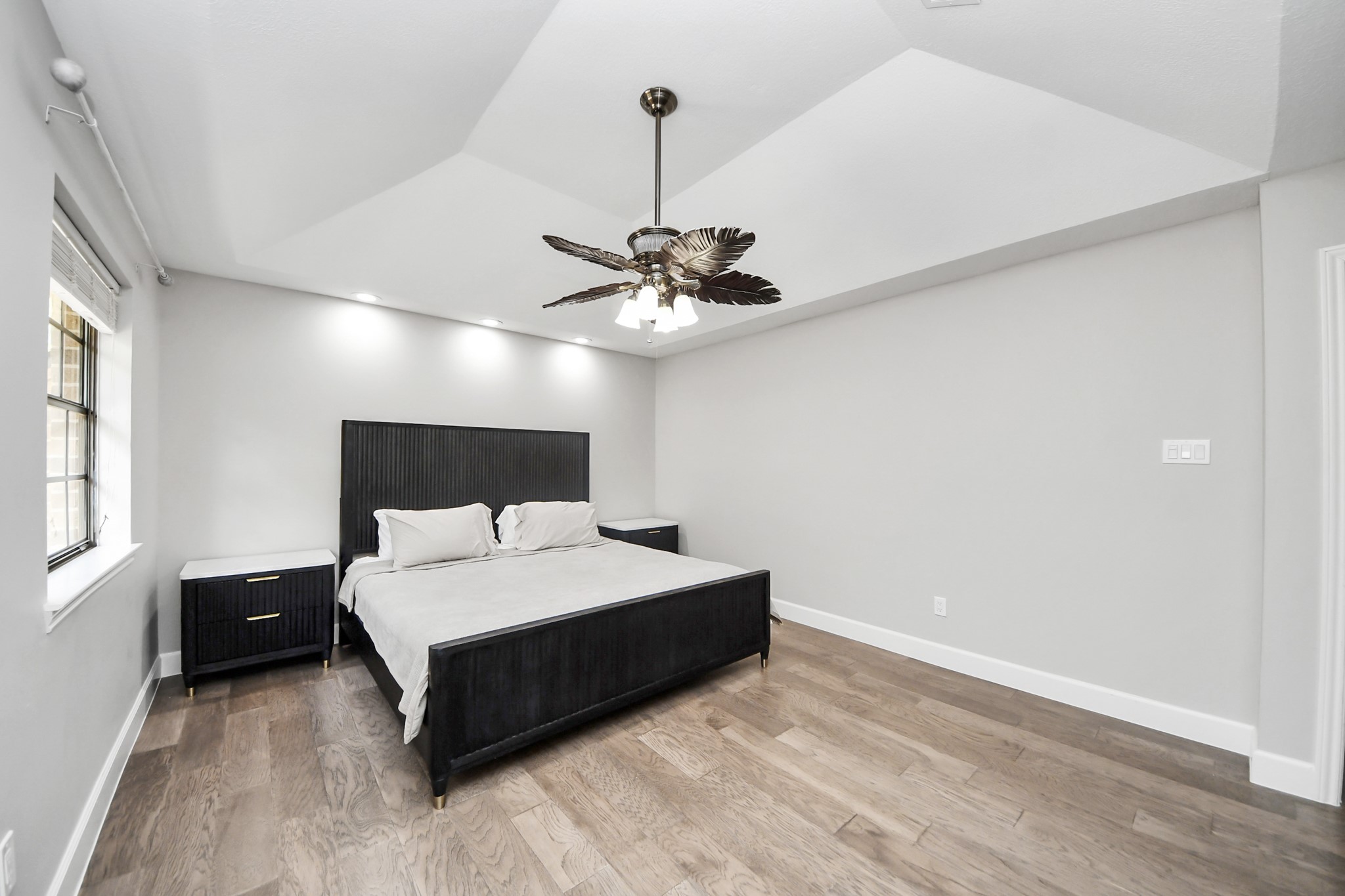 Spacious bedroom with sleek modern design, featuring a vaulted ceiling, elegant light fixture, and abundant natural light from the large window.