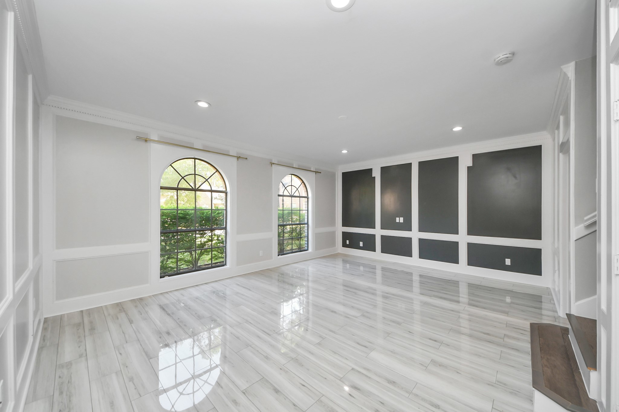 Bright and spacious formal living area featuring elegant arched windows, sleek tile flooring, and modern accent walls.