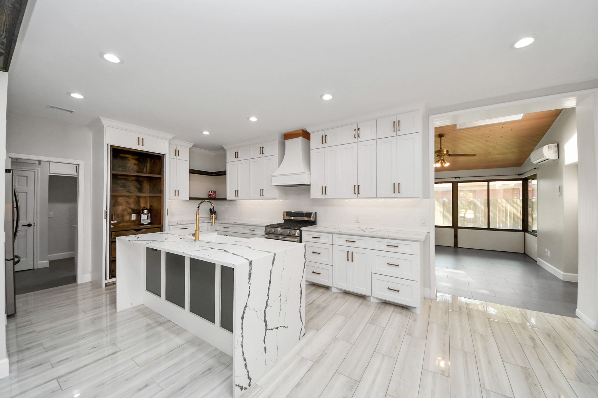 Sleek, modern kitchen with a striking waterfall island, elegant white cabinetry, and stainless steel appliances, seamlessly connected to a bright, inviting sunroom.