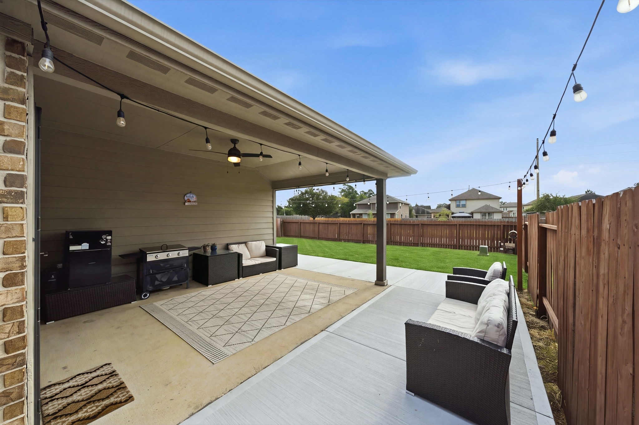 Charming covered patio with comfortable seating, perfect for entertaining, opens up to a spacious fenced backyard with lush greenery.
