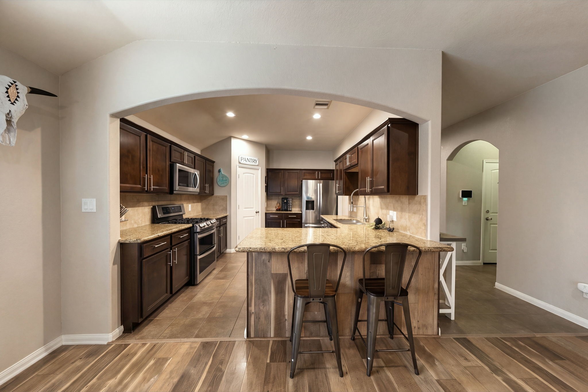 Spacious kitchen with rich wood cabinetry, granite countertops, and a central island with seating, complemented by stainless steel appliances and a cozy pantry nook.