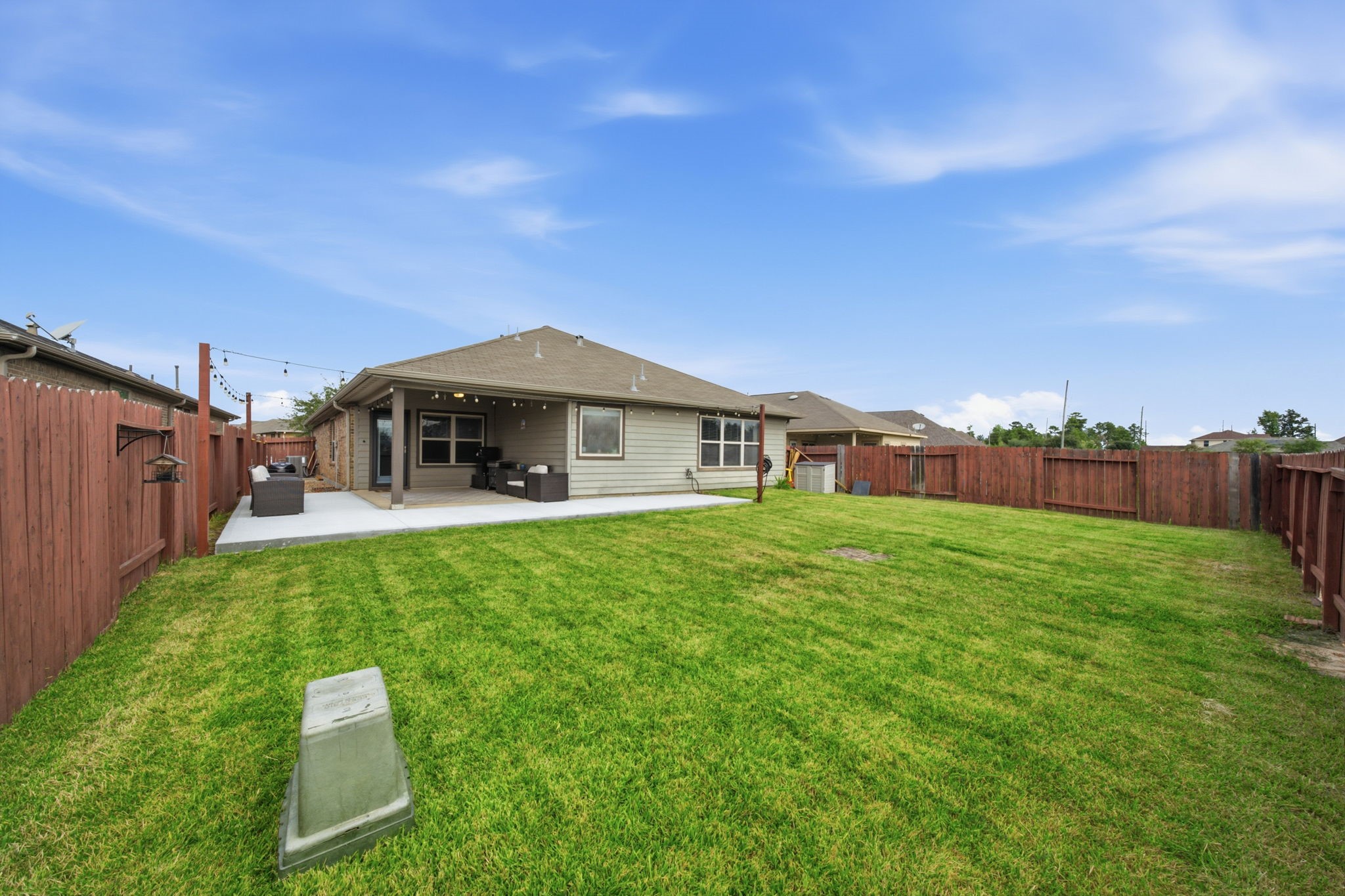 Spacious backyard with a well-maintained lawn, featuring a cozy covered patio perfect for outdoor gatherings, all enclosed by a charming wooden fence.
