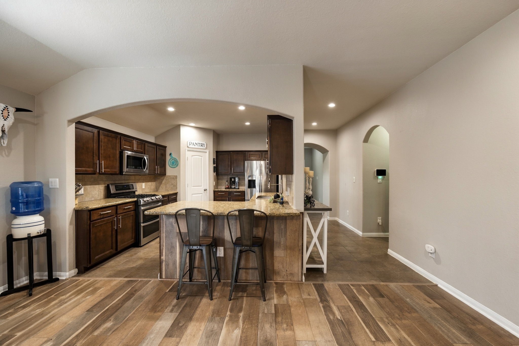 Charming kitchen with rich wood cabinetry, stainless steel appliances, and a cozy breakfast bar under a graceful archway.