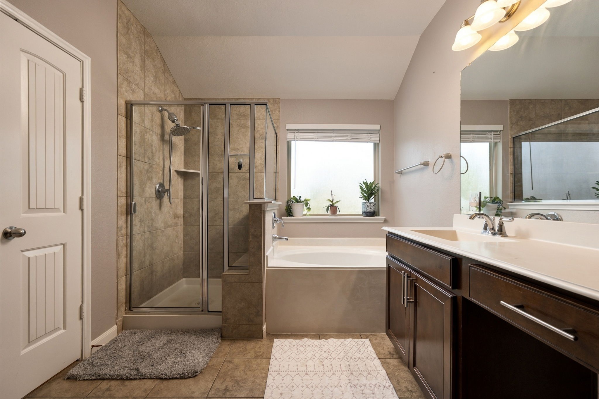 Spacious bathroom featuring a glass-enclosed shower, a luxurious soaking tub, and a dual-sink vanity with ample storage.