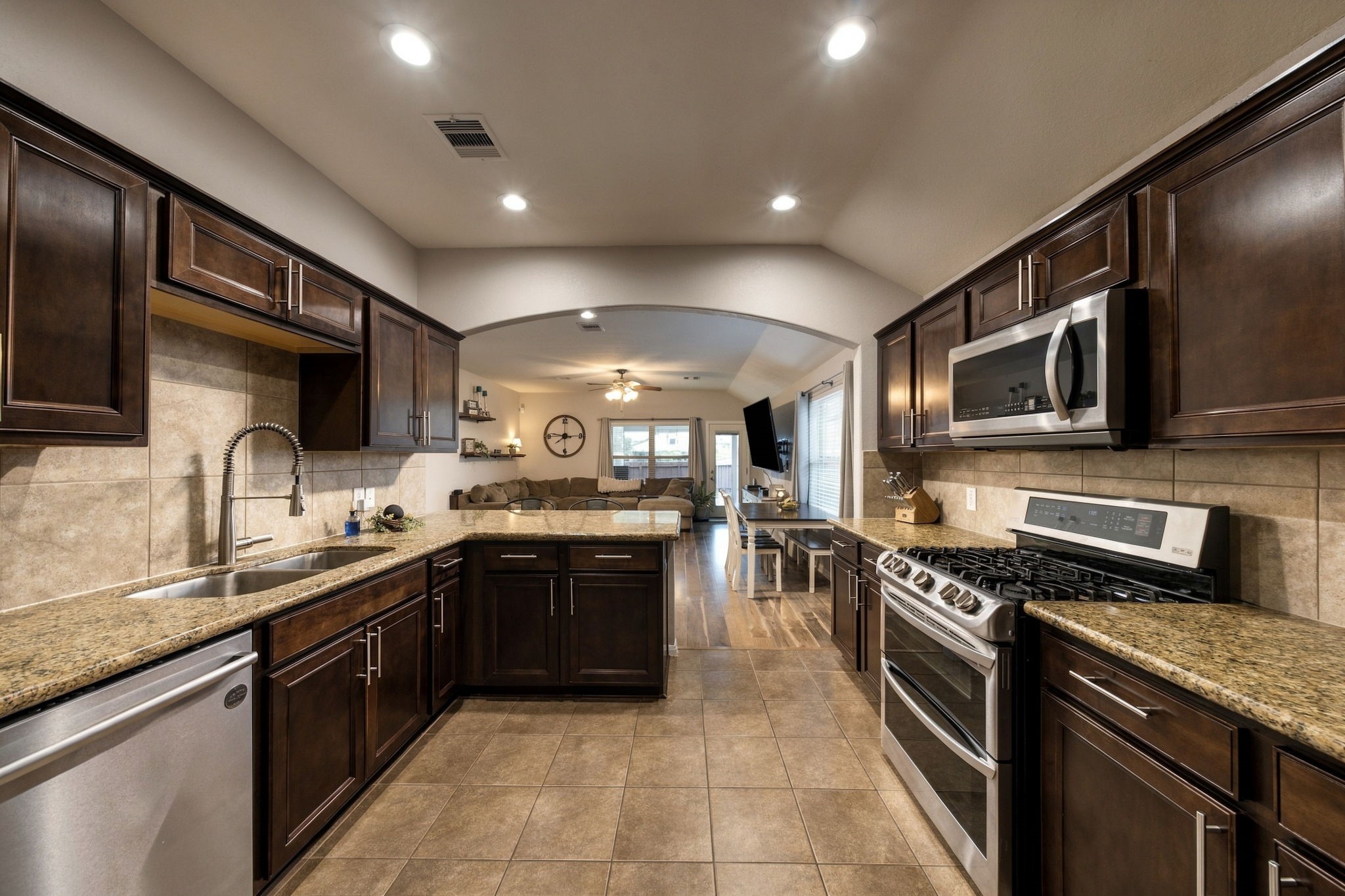 Spacious kitchen with rich dark wood cabinetry, granite countertops, modern stainless steel appliances, and a seamless flow into the inviting living area.
