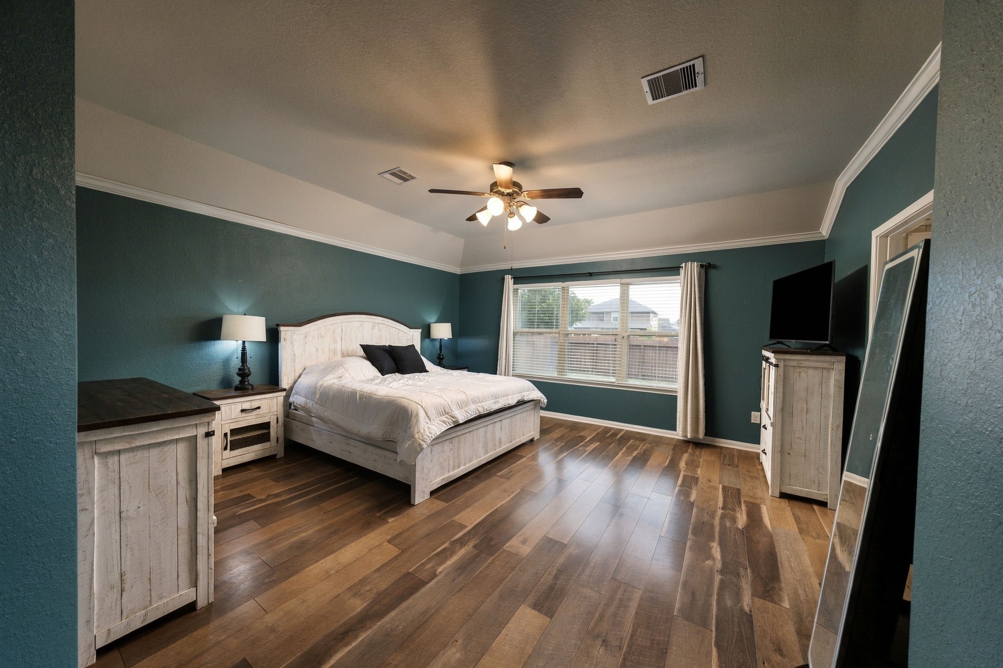 Spacious bedroom featuring rich wood flooring and abundant natural light from large windows.