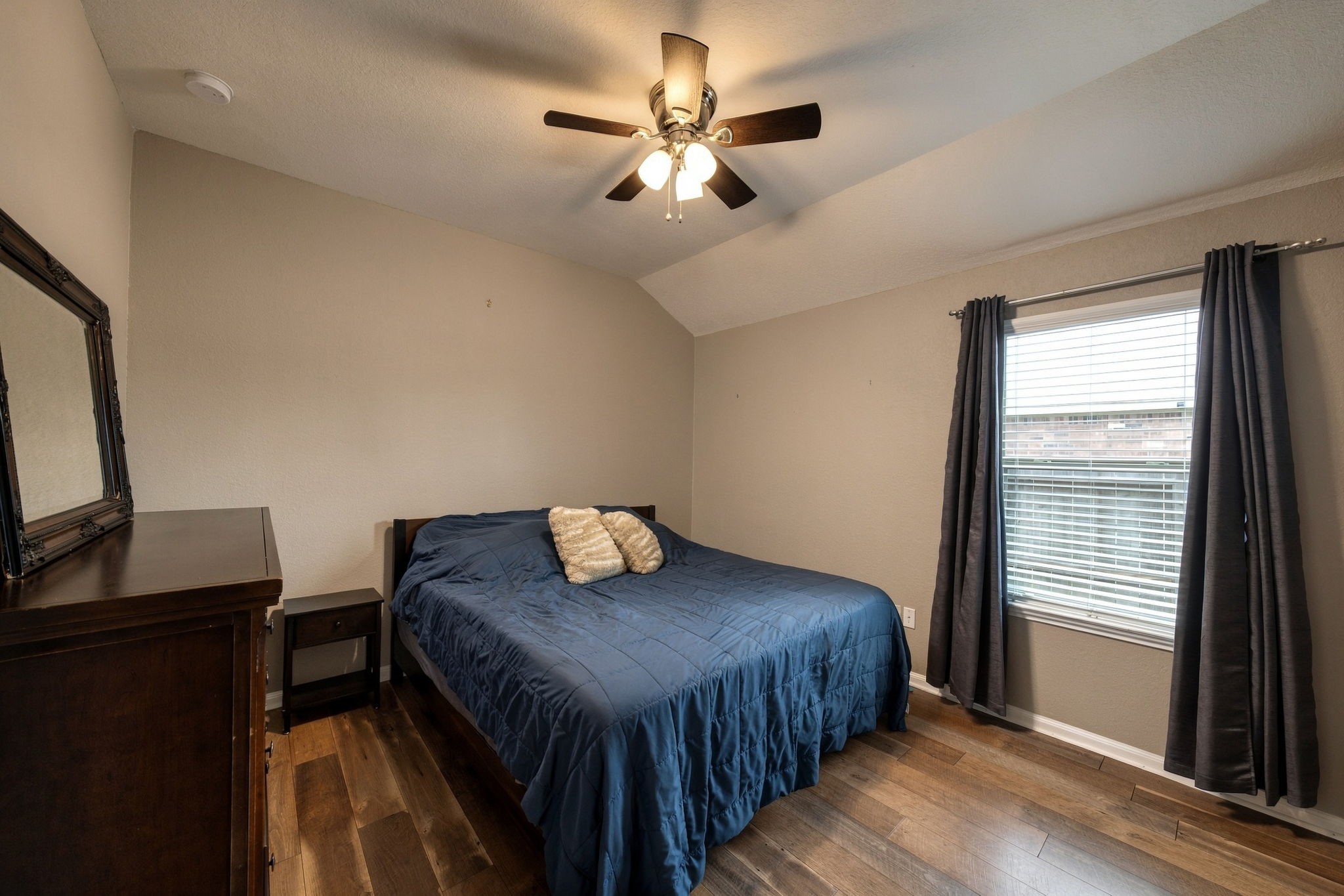 Cozy bedroom featuring warm wooden floors, a ceiling fan for comfort, and ample natural light through a large window.