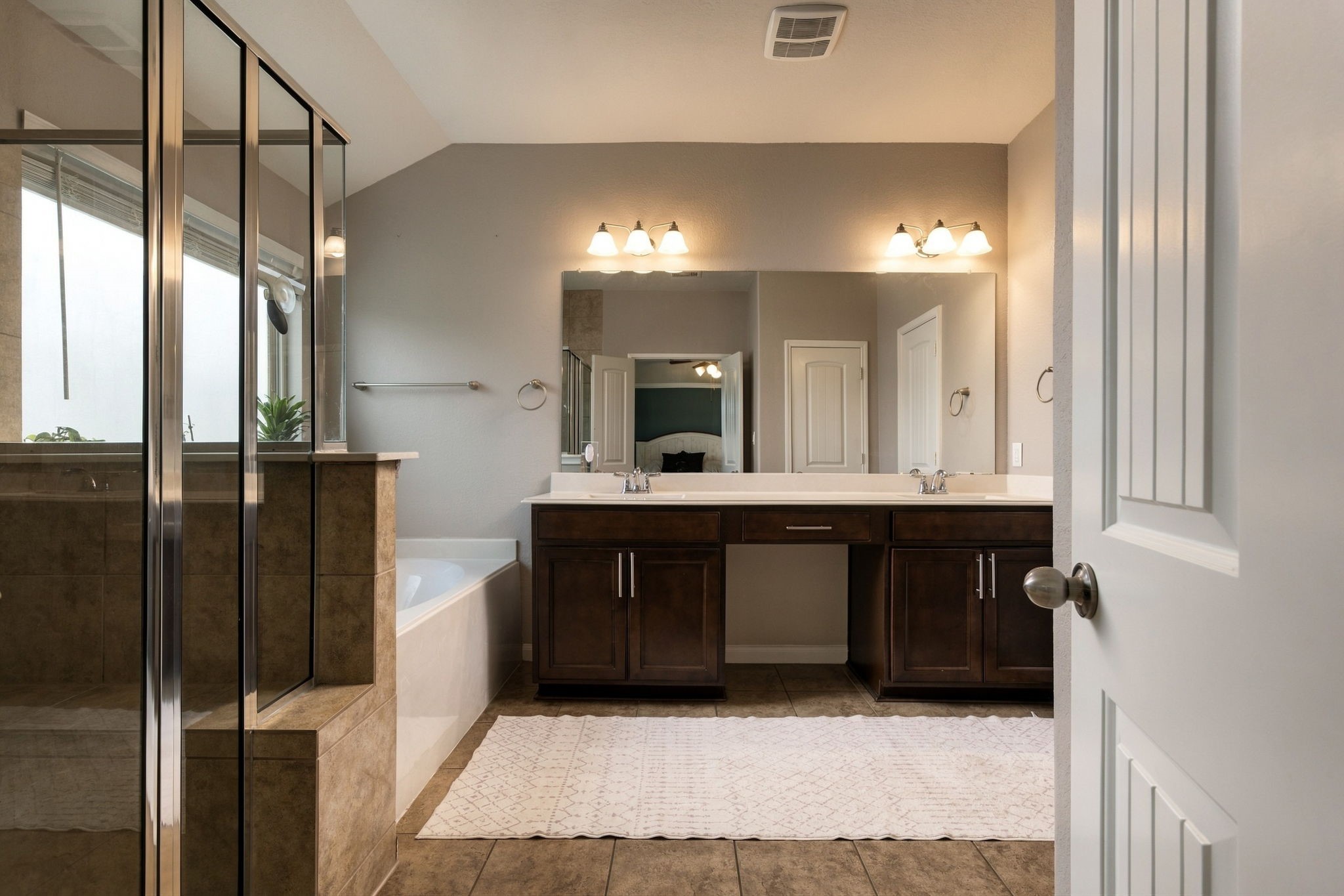 Spacious bathroom featuring a double vanity with elegant lighting, a large mirror, and a glass-enclosed shower next to a relaxing bathtub.