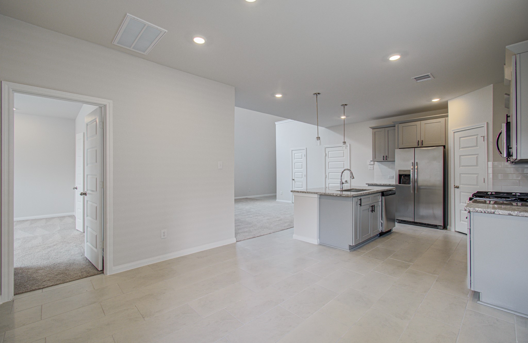 Modern open-concept kitchen with sleek stainless steel appliances, granite countertops, and stylish pendant lighting, seamlessly flowing into a spacious living area and adjacent room. Please Note this is a different home/floorplan in the community.