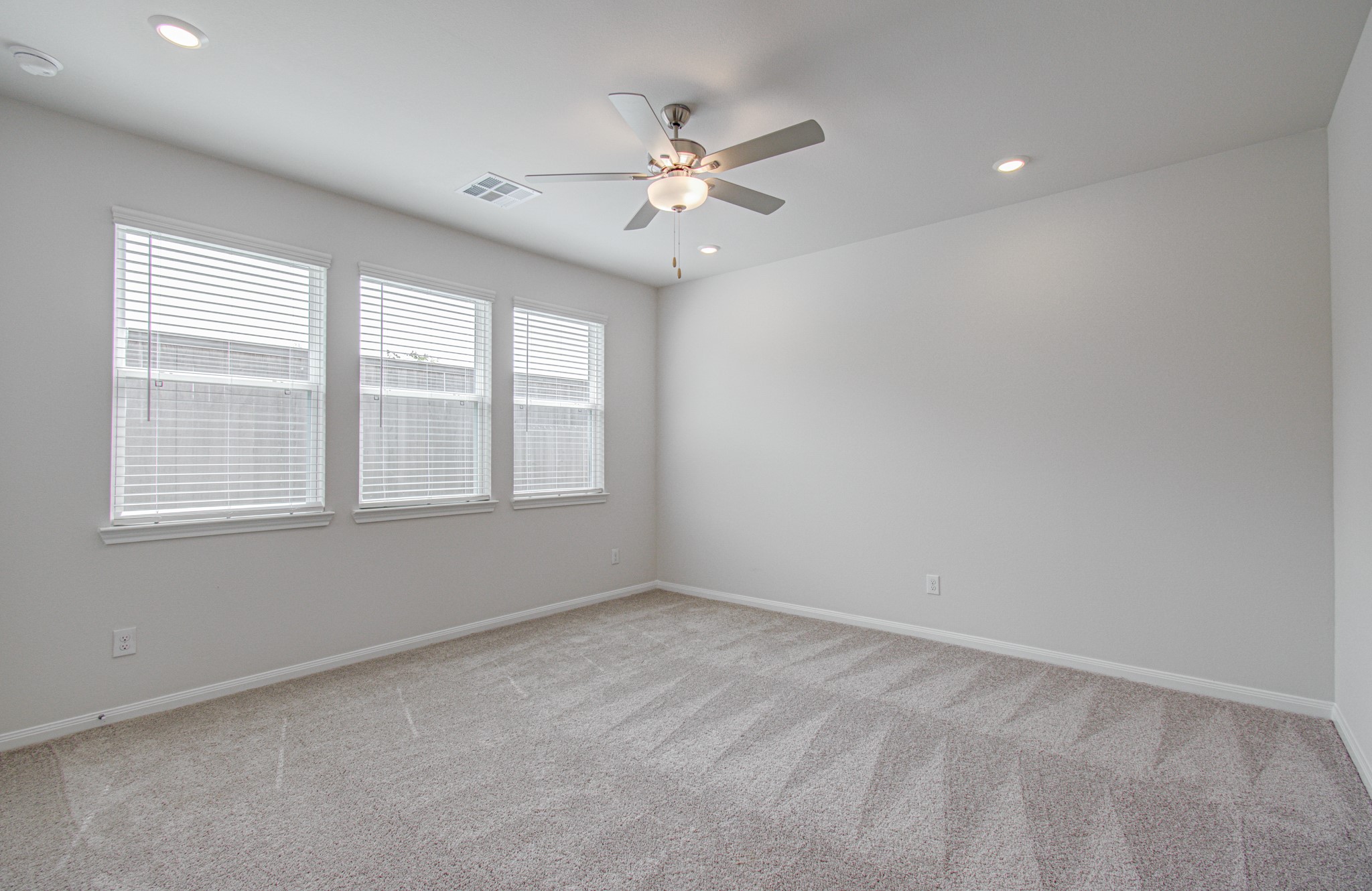Bright and spacious game-room featuring a ceiling fan, plush carpet, and ample natural light from three large windows. Please Note this is a different home/floorplan in the community.