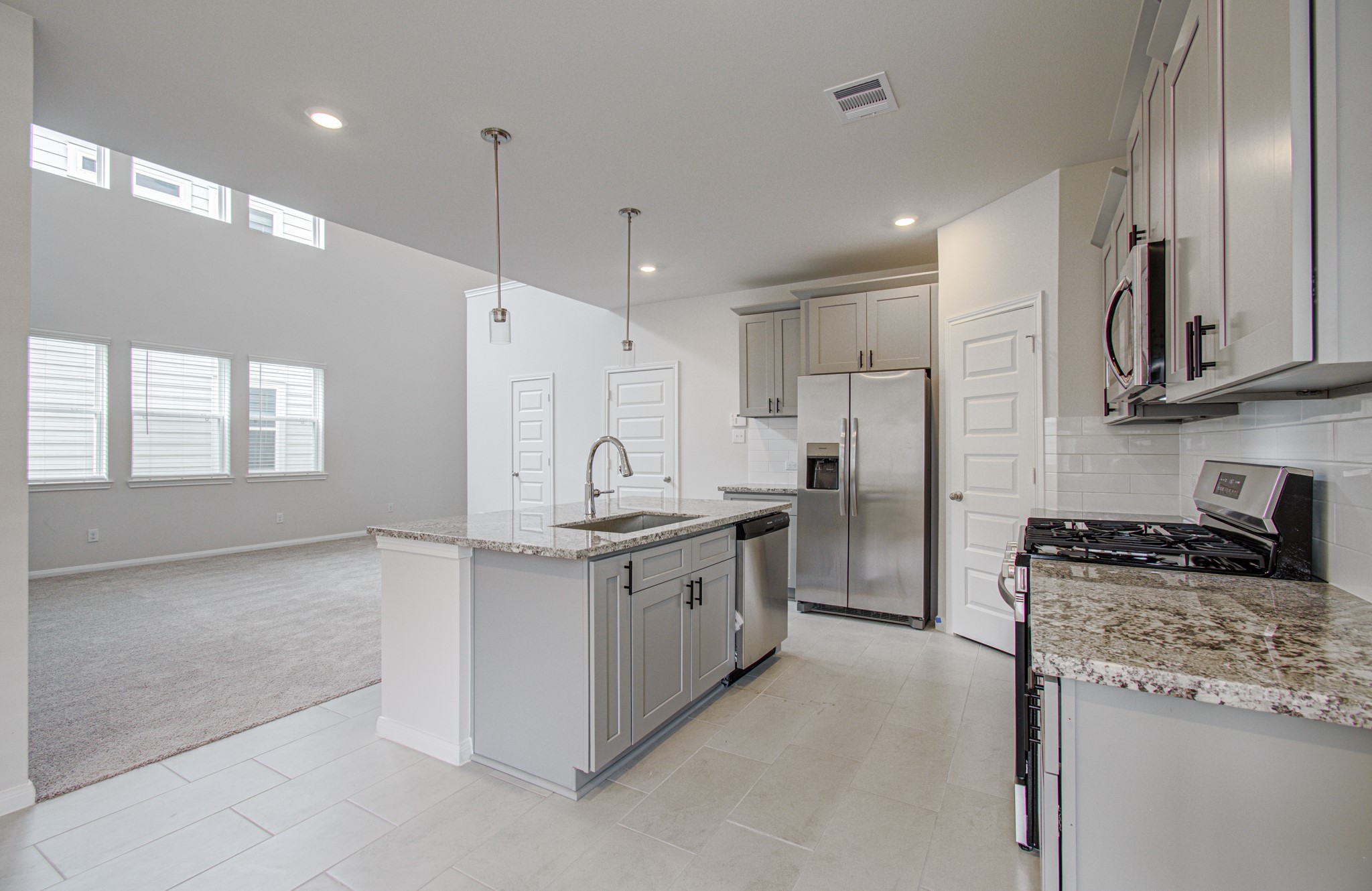 Modern kitchen with granite countertops, stainless steel appliances, and ample cabinetry, seamlessly flowing into a bright, open living area with large windows. Please Note this is a different home/floorplan in the community.
