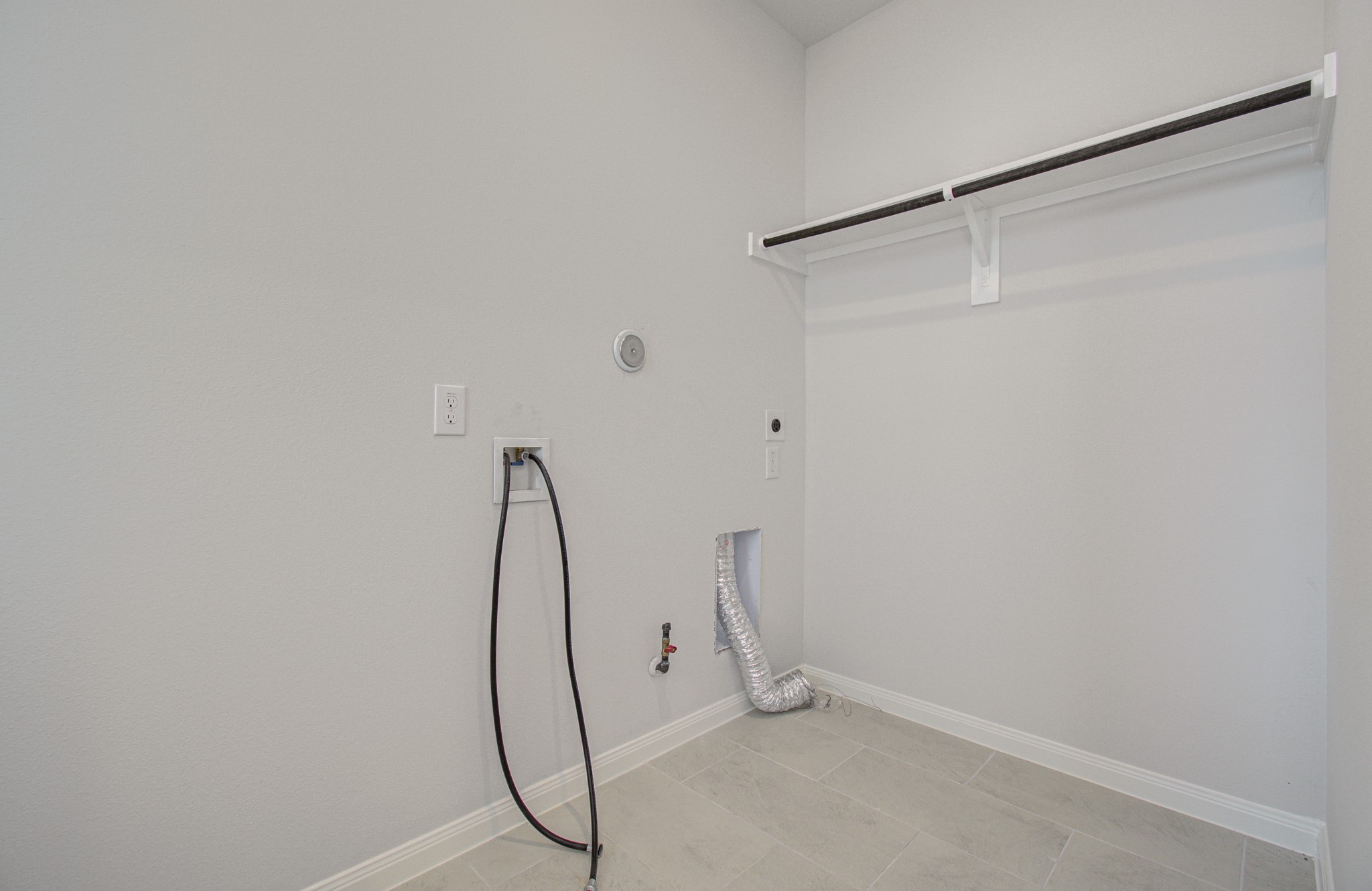 Spacious laundry room featuring washer and dryer hookups, a convenient utility shelf, and tiled flooring for easy maintenance. Please Note this is a different home/floorplan in the community.