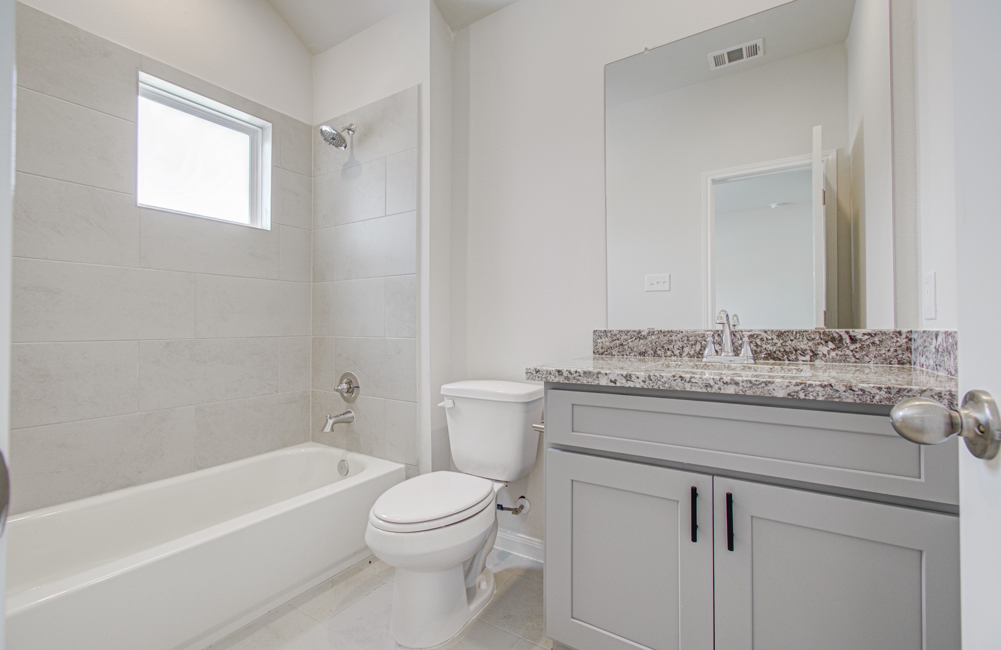 Modern secondary bathroom featuring a sleek granite countertop, elegant gray cabinetry, and a spacious bathtub with stylish tile surround. Please Note this is a different home/floorplan in the community.