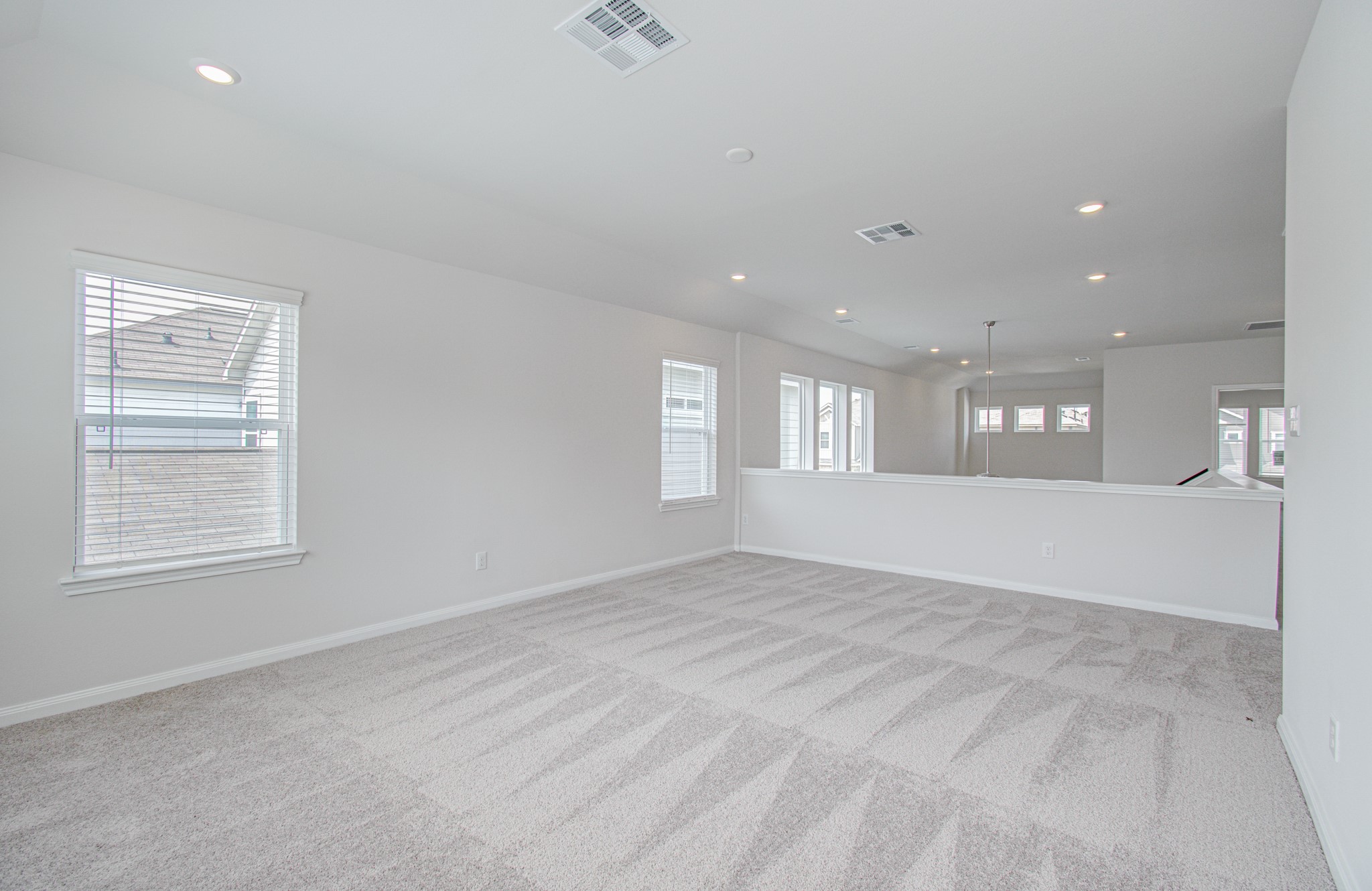 Spacious and bright open-concept game-room loft area with plush carpeting, ample natural light from multiple windows, and recessed lighting for a modern touch. Please Note this is a different home/floorplan in the community.