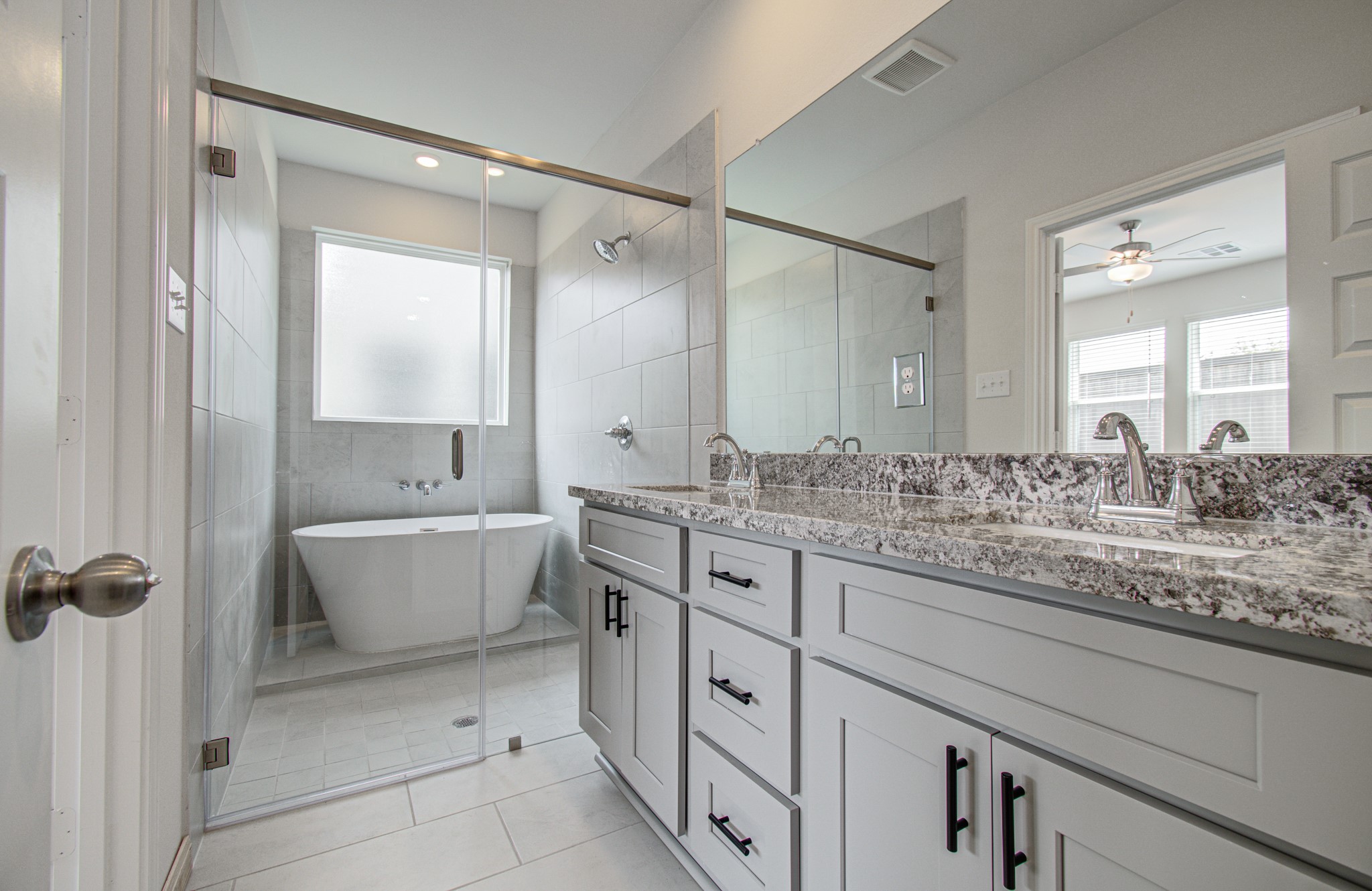 Elegant primary bathroom featuring a spacious glass-enclosed shower and a luxurious soaking tub, complemented by a sleek double vanity with granite countertops. Please Note this is a different home/floorplan in the community.