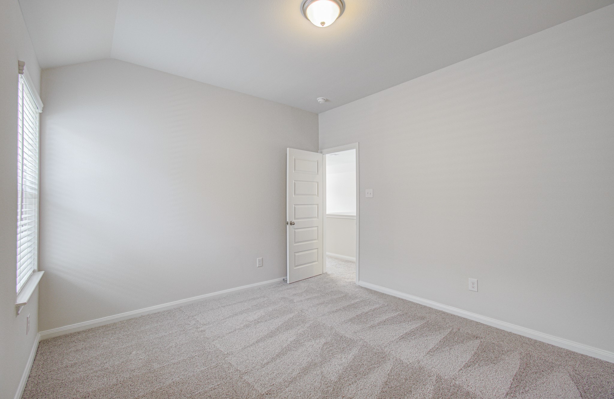Bright and inviting fourth bedroom with plush carpeting and a soft neutral color palette, featuring a large window that fills the space with natural light. Please Note this is a different home/floorplan in the community.