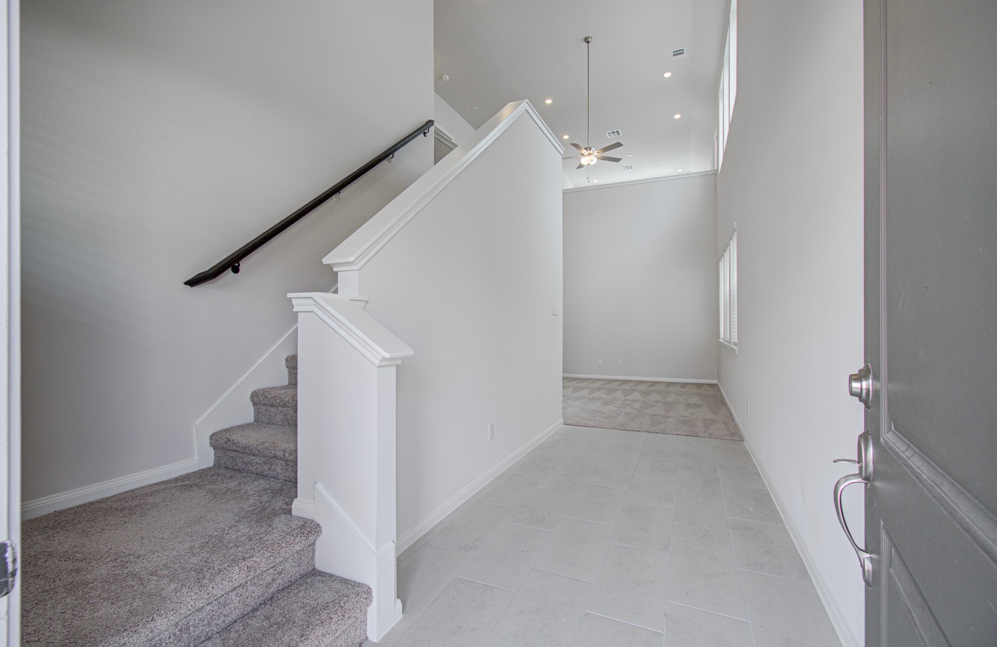 Bright entryway with high ceilings, leading to a cozy carpeted staircase and an open living area. Please Note this is a different home/floorplan in the community.