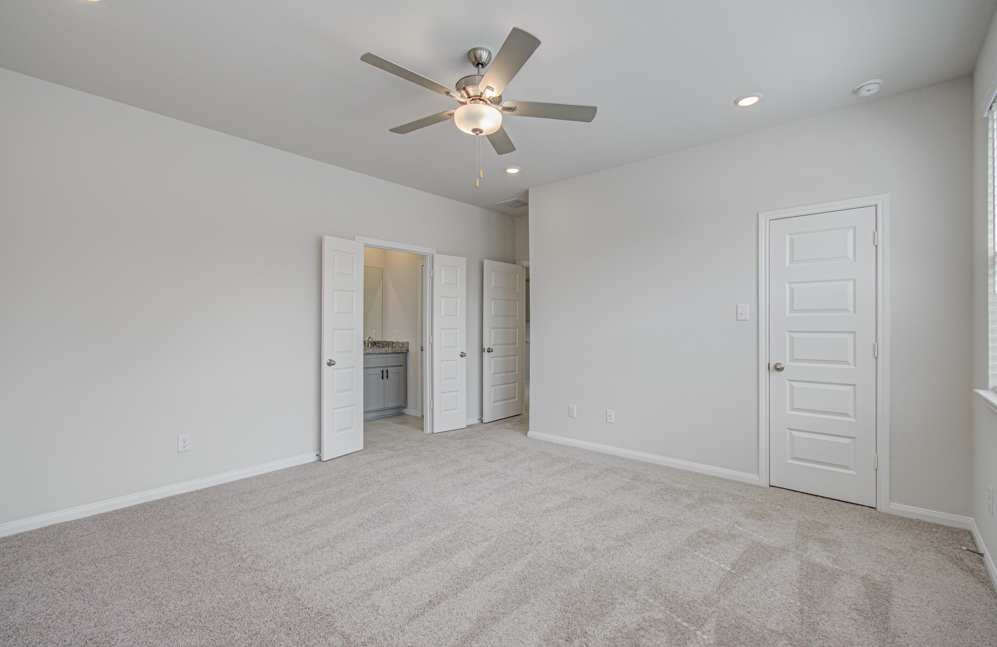 Spacious primary bedroom with plush carpeting, neutral tones, a ceiling fan, and convenient en-suite bathroom access. Please Note this is a different home/floorplan in the community.