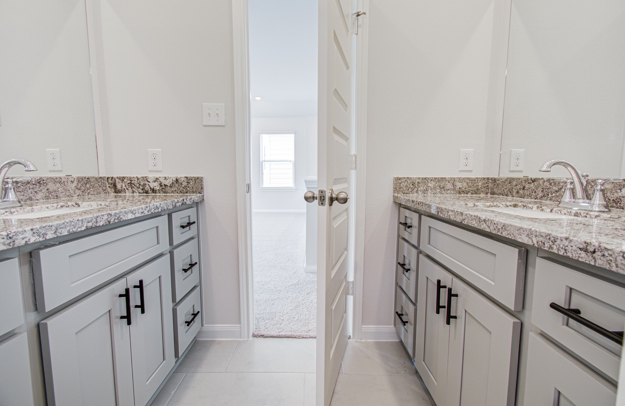 Elegant dual vanity third bathroom with granite countertops and sleek cabinetry, leading into a bright, inviting room. Please Note this is a different home/floorplan in the community.