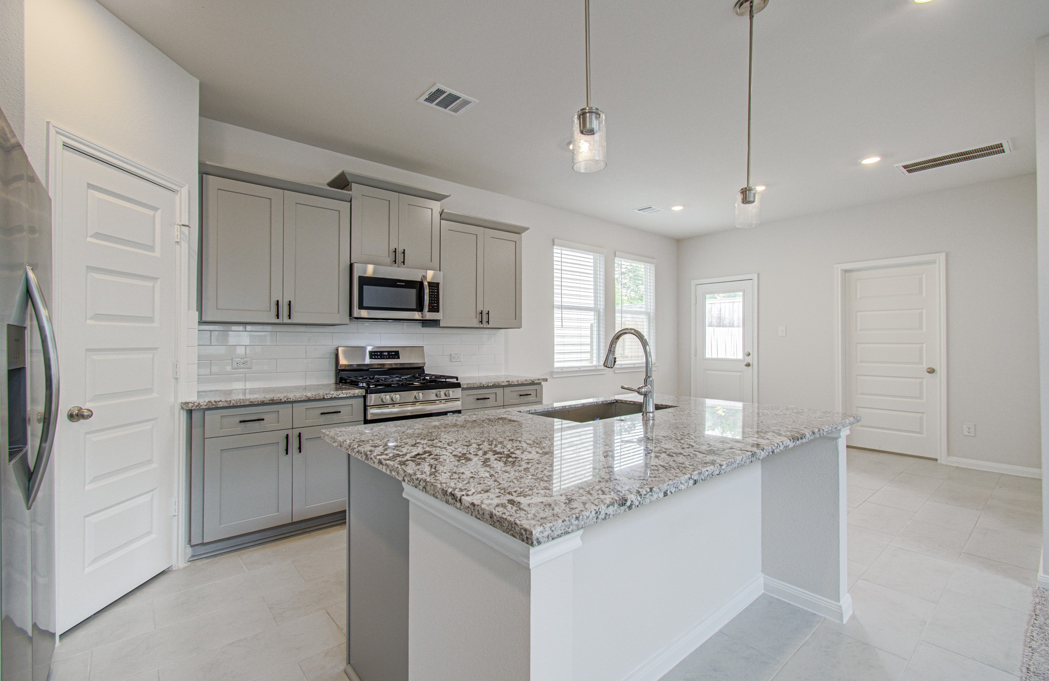 Modern kitchen with sleek granite countertops, stainless steel appliances, and stylish gray cabinetry, offering ample natural light and a functional open layout. Please Note this is a different home/floorplan in the community.