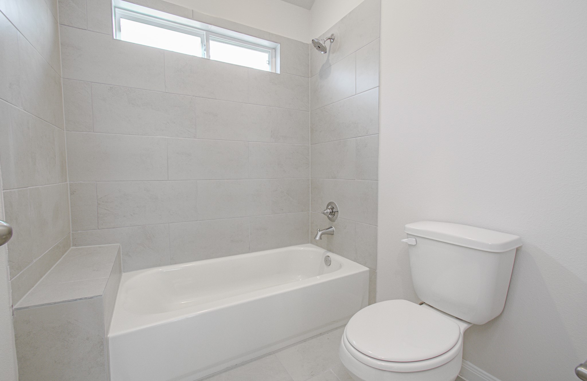 Bright and modern bathroom featuring a sleek bathtub with overhead shower, elegant tile work, and ample natural light. Please Note this is a different home/floorplan in the community.