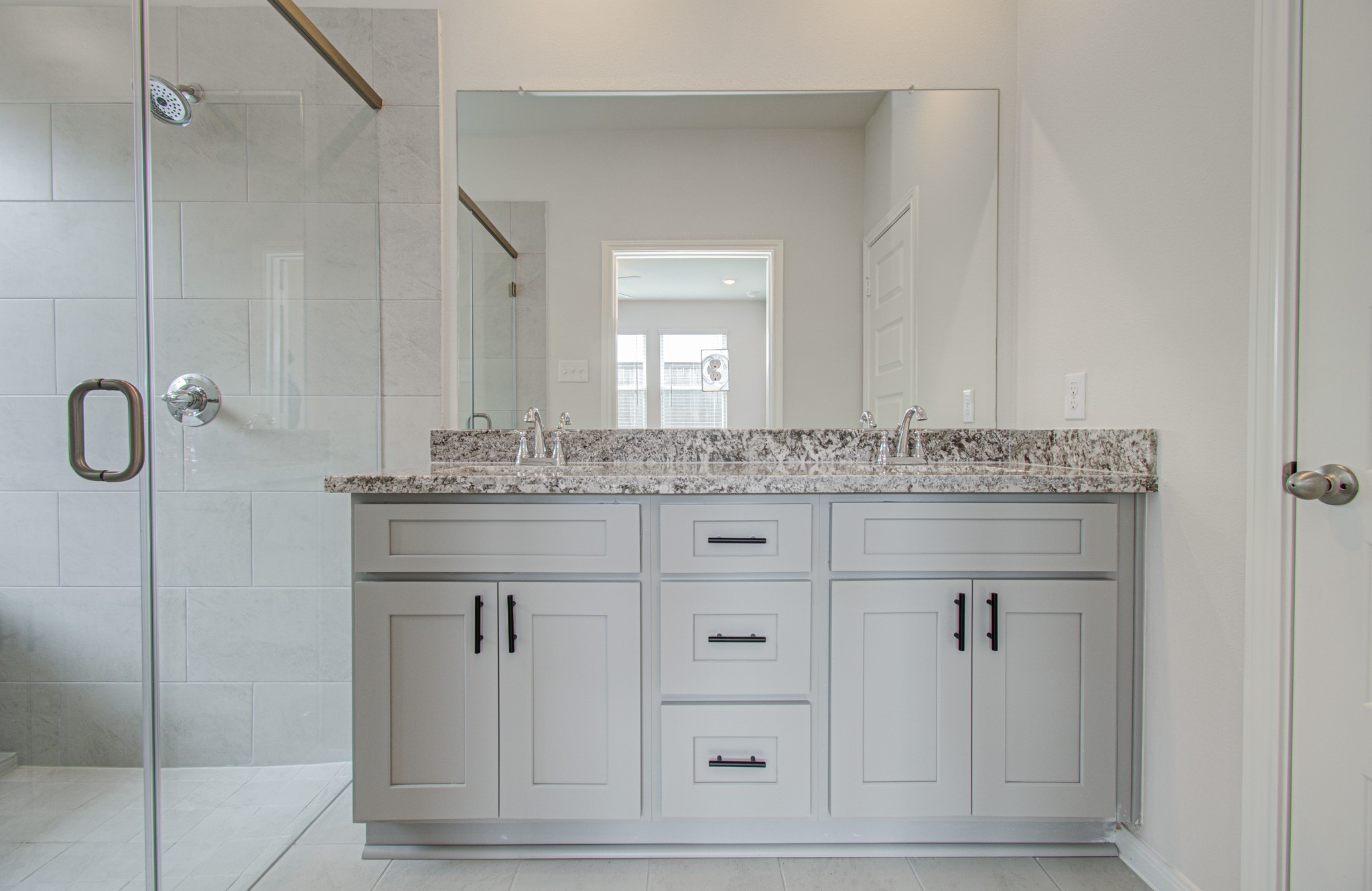 Elegant primary bathroom featuring a sleek double vanity with granite countertops and a spacious glass-enclosed shower. Please Note this is a different home/floorplan in the community.
