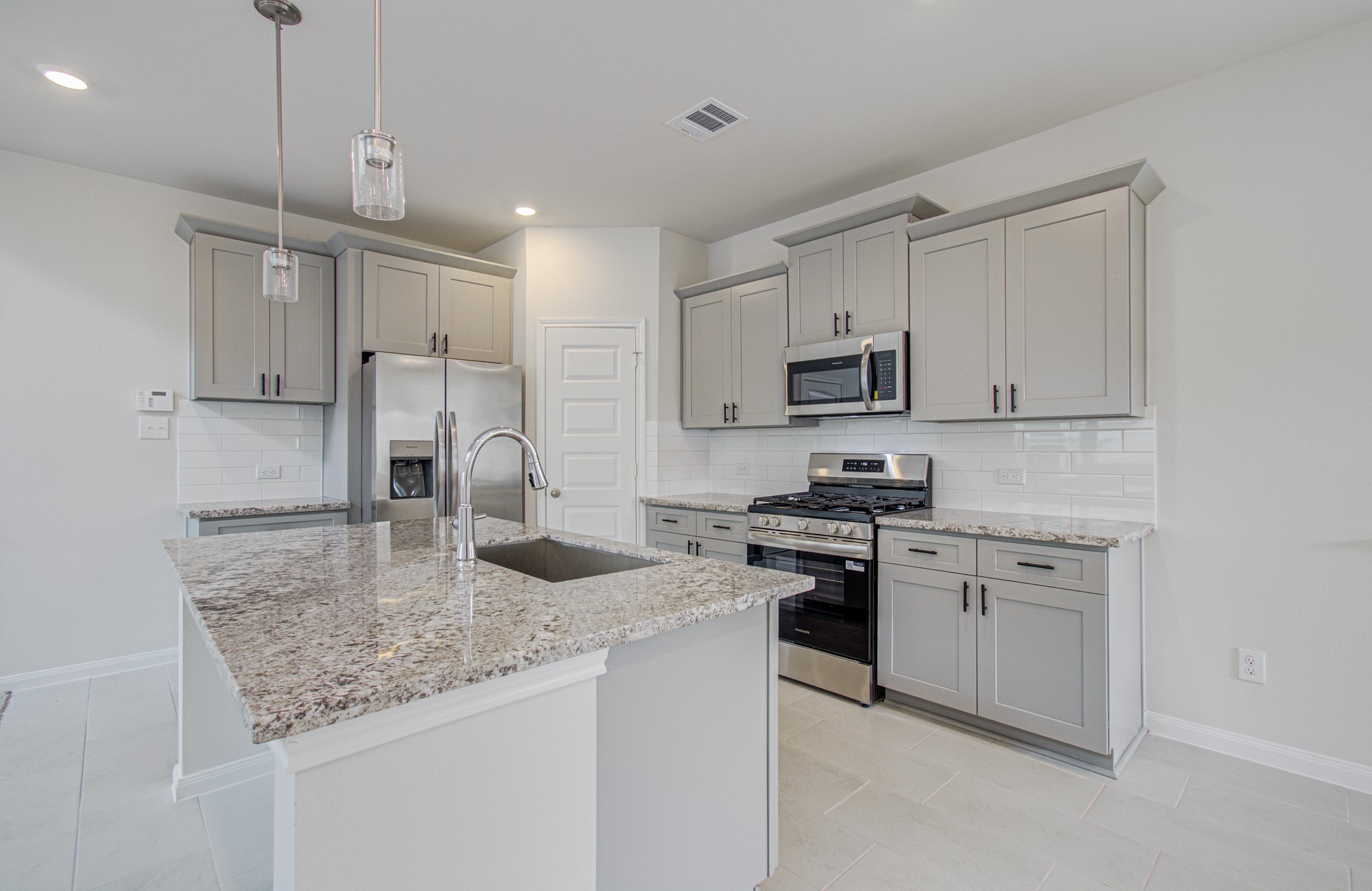Modern kitchen with sleek granite countertops, stainless steel appliances, and elegant gray cabinetry, offering a stylish and functional space. Please Note this is a different home/floorplan in the community.