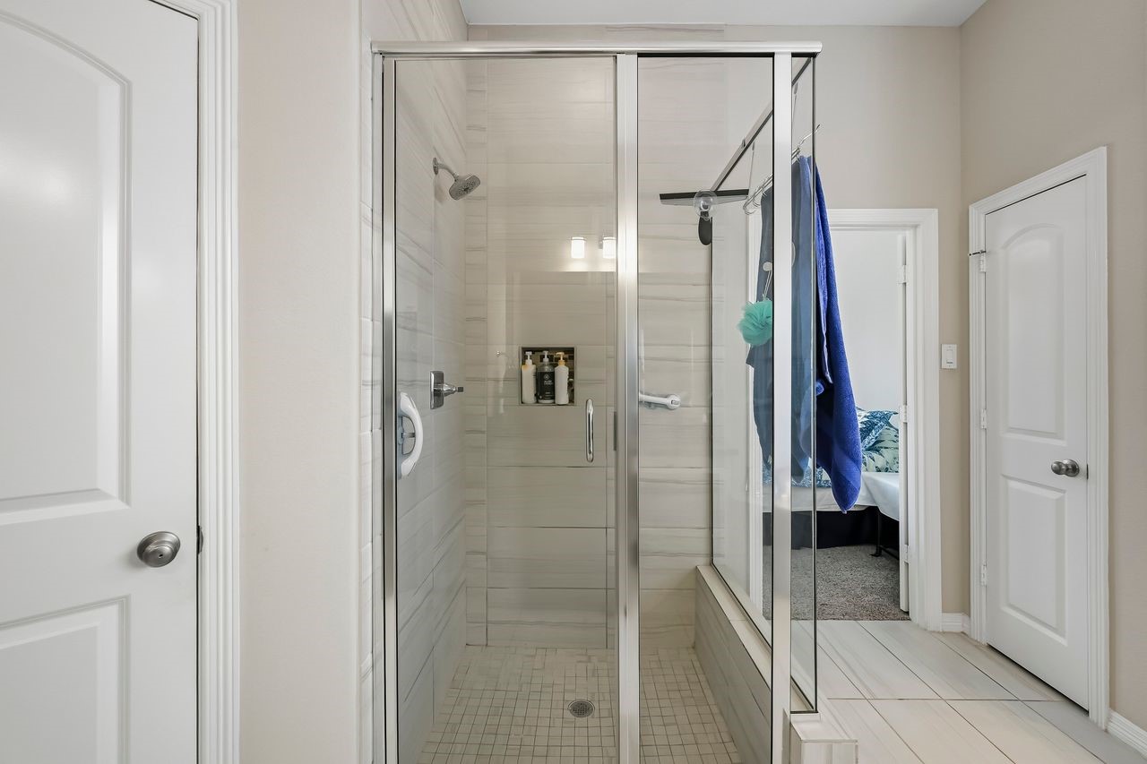 A sophisticated primary ensuite featuring a seamless glass shower enclosure, complemented by floor-to-ceiling tiling and refined fixtures in a timeless neutral finish.