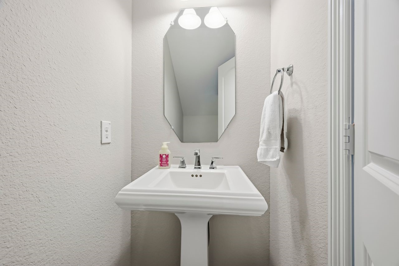 Sophisticated and serene, this guest powder room features a classic white porcelain pedestal sink complemented by neutral tones, refined wall-mounted lighting, and a polished mirror.