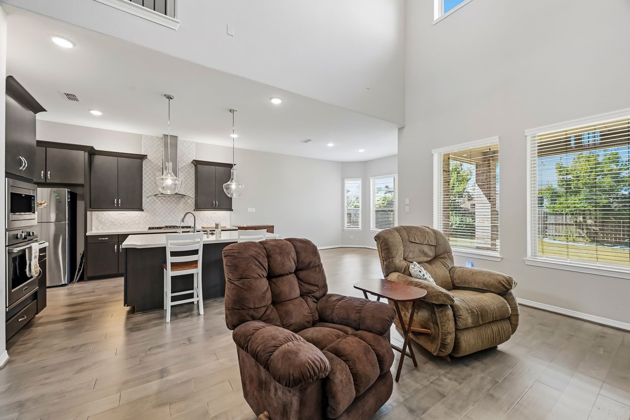 This expansive open-concept space centers around a sleek kitchen island topped with crisp quartz, complemented by sophisticated dark cabinetry and a premium gas cooktop. High-end stainless steel appliances and a reverse osmosis system add modern convenience, while soaring ceilings and oversized windows flood the area with natural light, creating a seamless blend of contemporary style and effortless functionality.