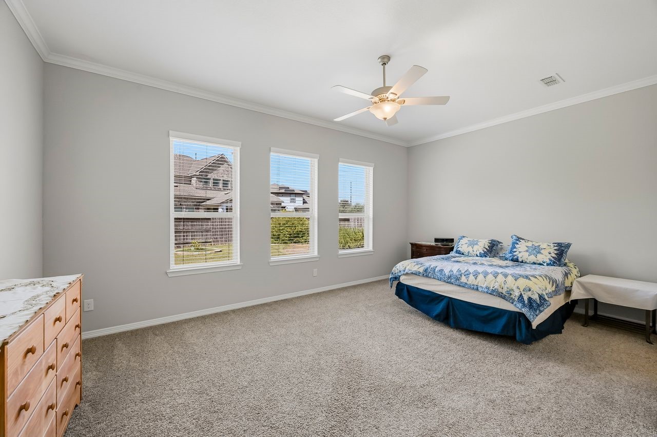 Step into the primary retreat, where elegant crown molding and expansive windows frame a serene view of the lushly landscaped grounds. This spacious sanctuary is complete with a cooling ceiling fan and an abundance of natural light.