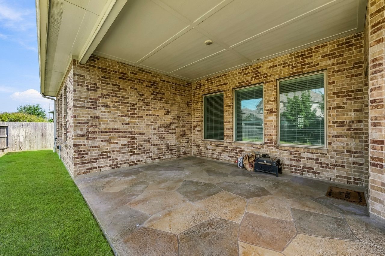 This expansive covered patio features elegant stone-patterned flooring and offers a serene vantage point over the meticulously landscaped grounds and tranquil water feature.