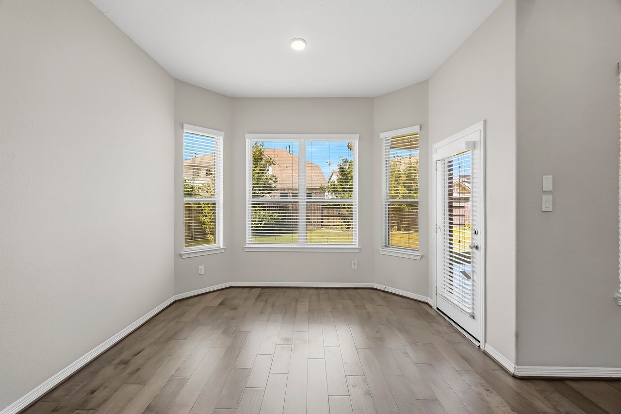 Bathed in natural light, this elegant breakfast bay features rich wood flooring and offers a seamless visual connection to the manicured landscaping and covered patio just beyond the glass.