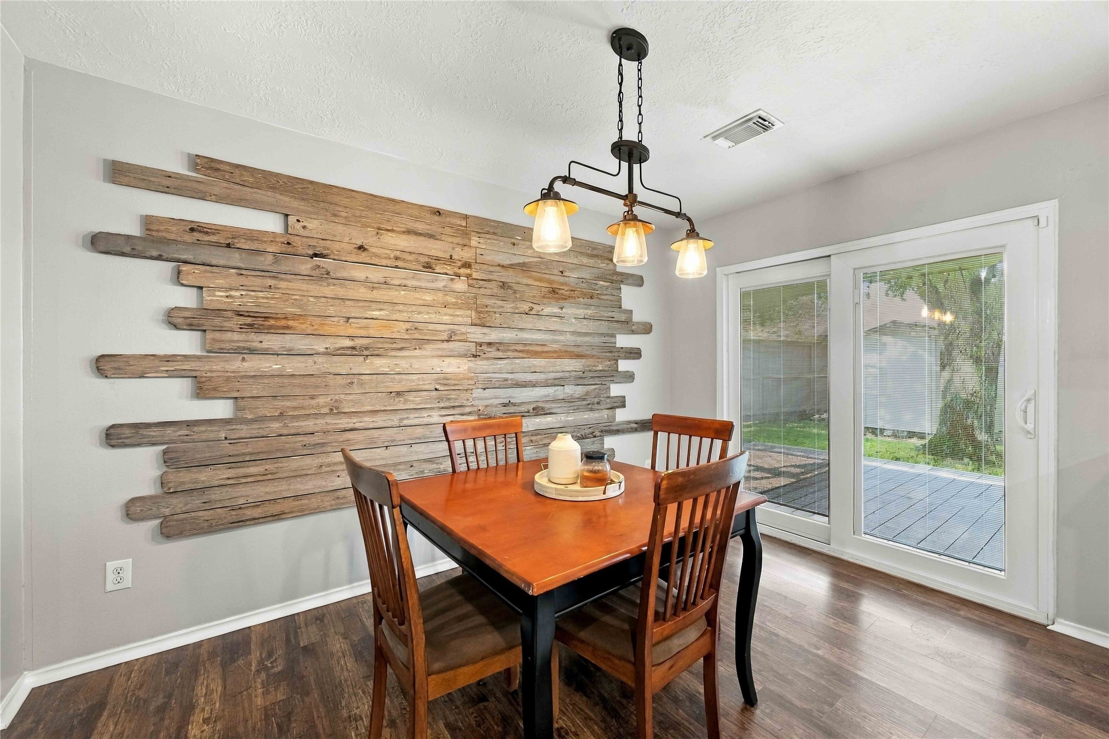 Dining area accented by a distinctive reclaimed-wood feature wall, statement lighting, and sliding glass doors opening to the outdoor living space.