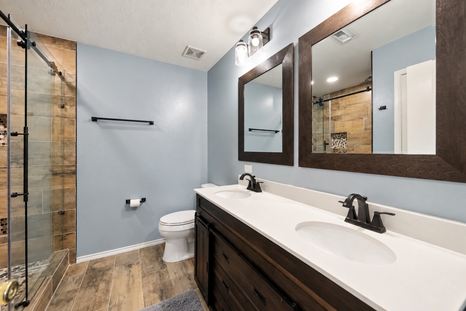 Updated primary bathroom features a long dual-sink vanity, contemporary fixtures, and a glass-enclosed walk-in shower.