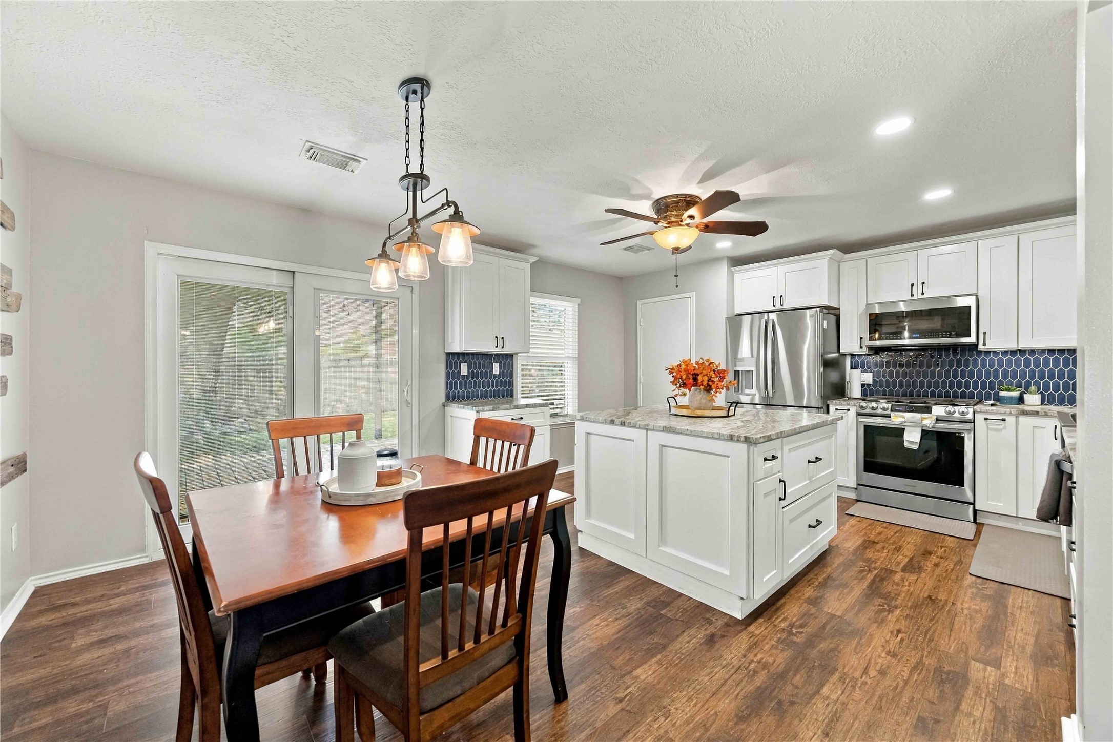 Updated kitchen and dining area featuring a large center island, white cabinetry, stainless-steel appliances, and direct access to the backyard deck. Updated kitchen and dining area featuring a large center island, white cabinetry, stainless-steel appliances, and direct access to the backyard deck.