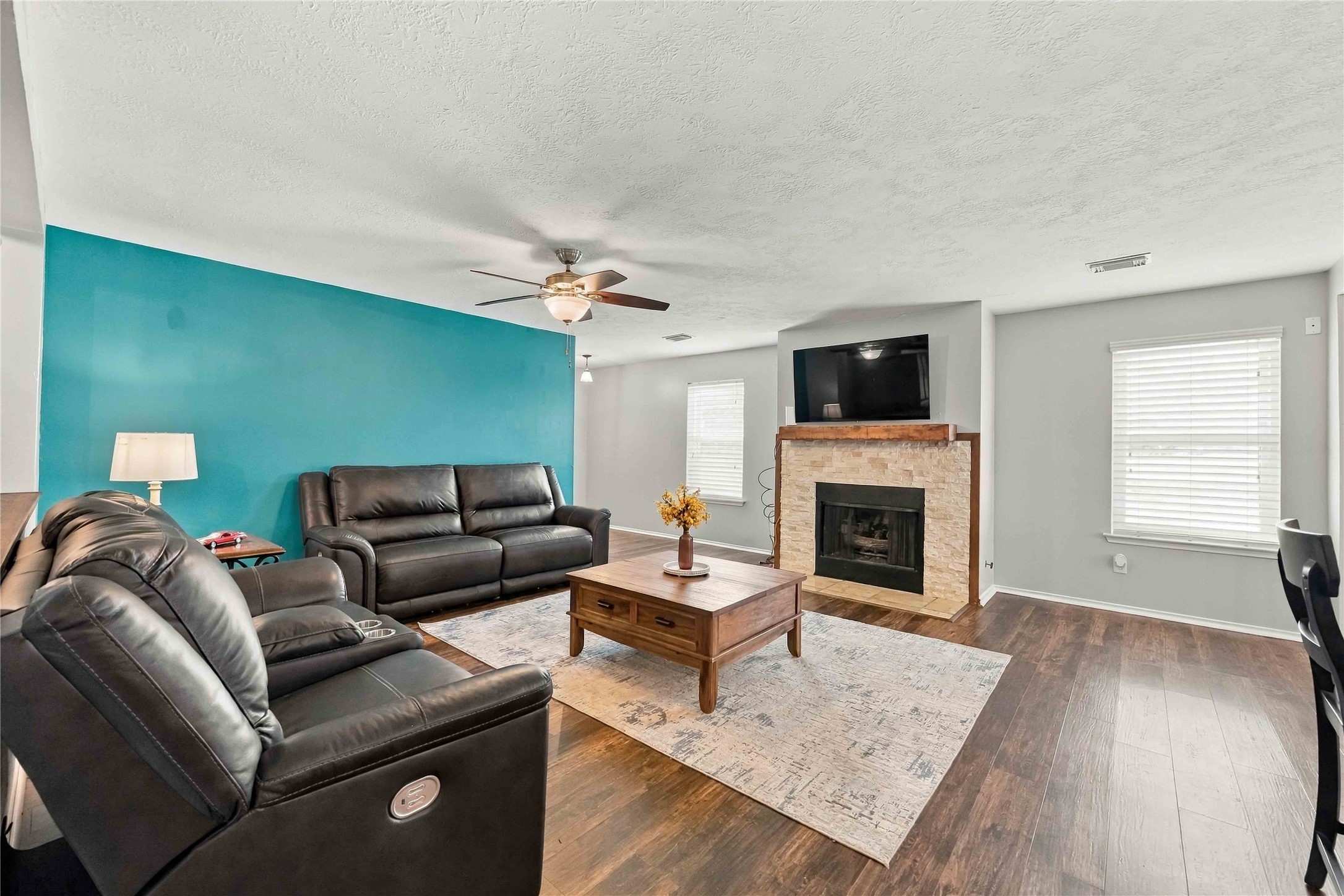 Generous living room featuring a stone-surround fireplace, natural light, and an open layout with ample floor space.